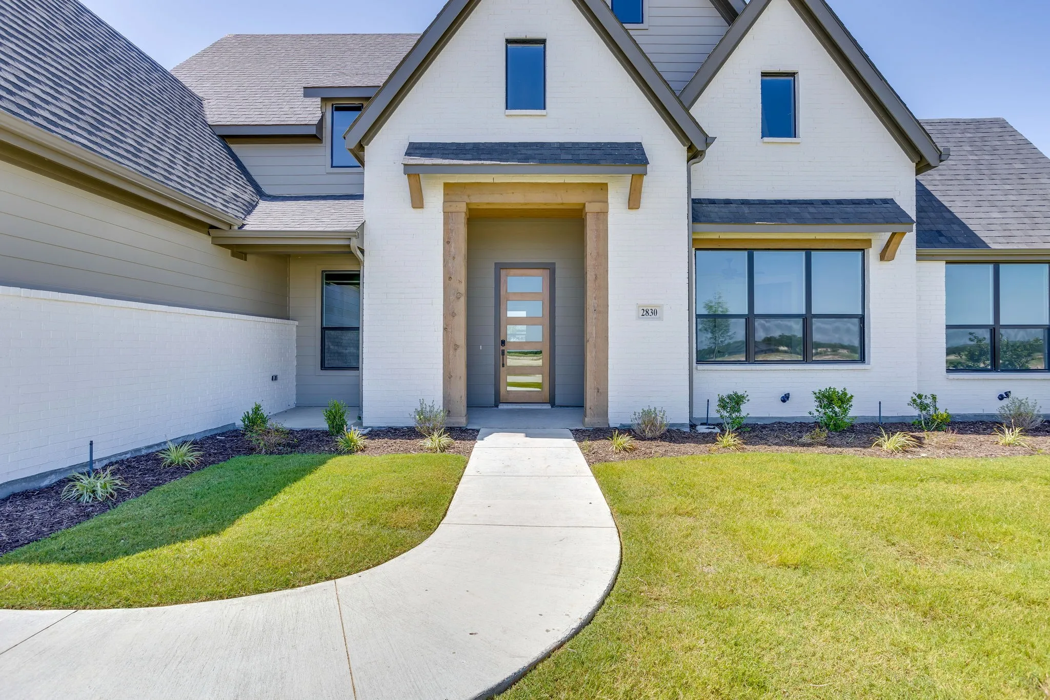 Contemporary exterior featuring painted brick and siding, a covered entry with wood beams, a modern front door, and dark-framed windows