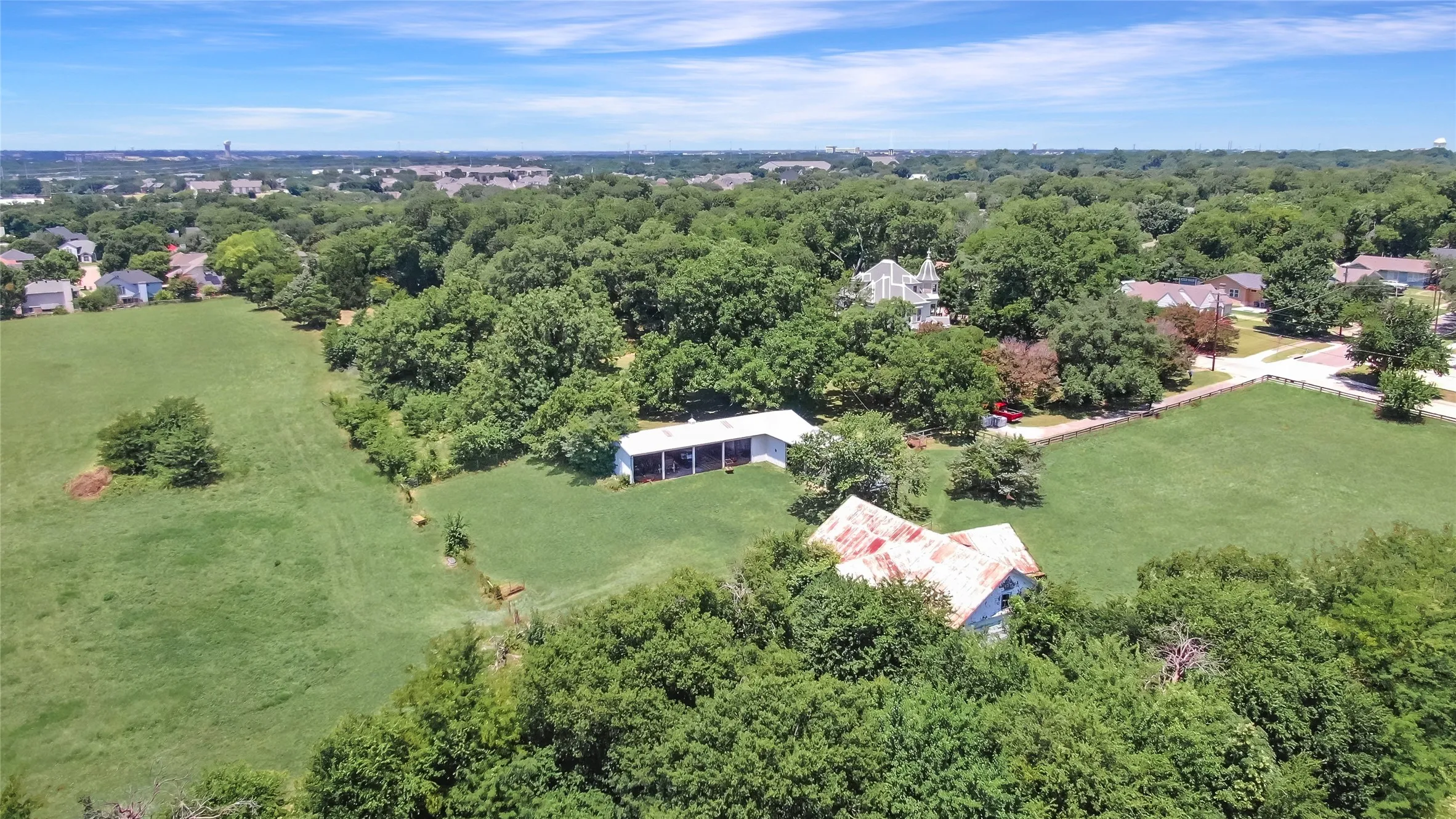 Expansive green pastures featuring mature trees and a distant residential area