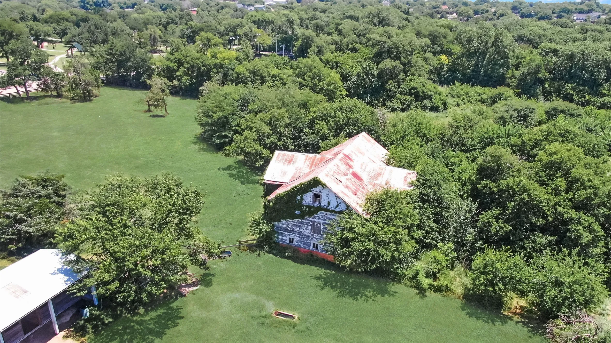 Expansive green space featuring a structure with a reddish-orange roof and a distressed exterior