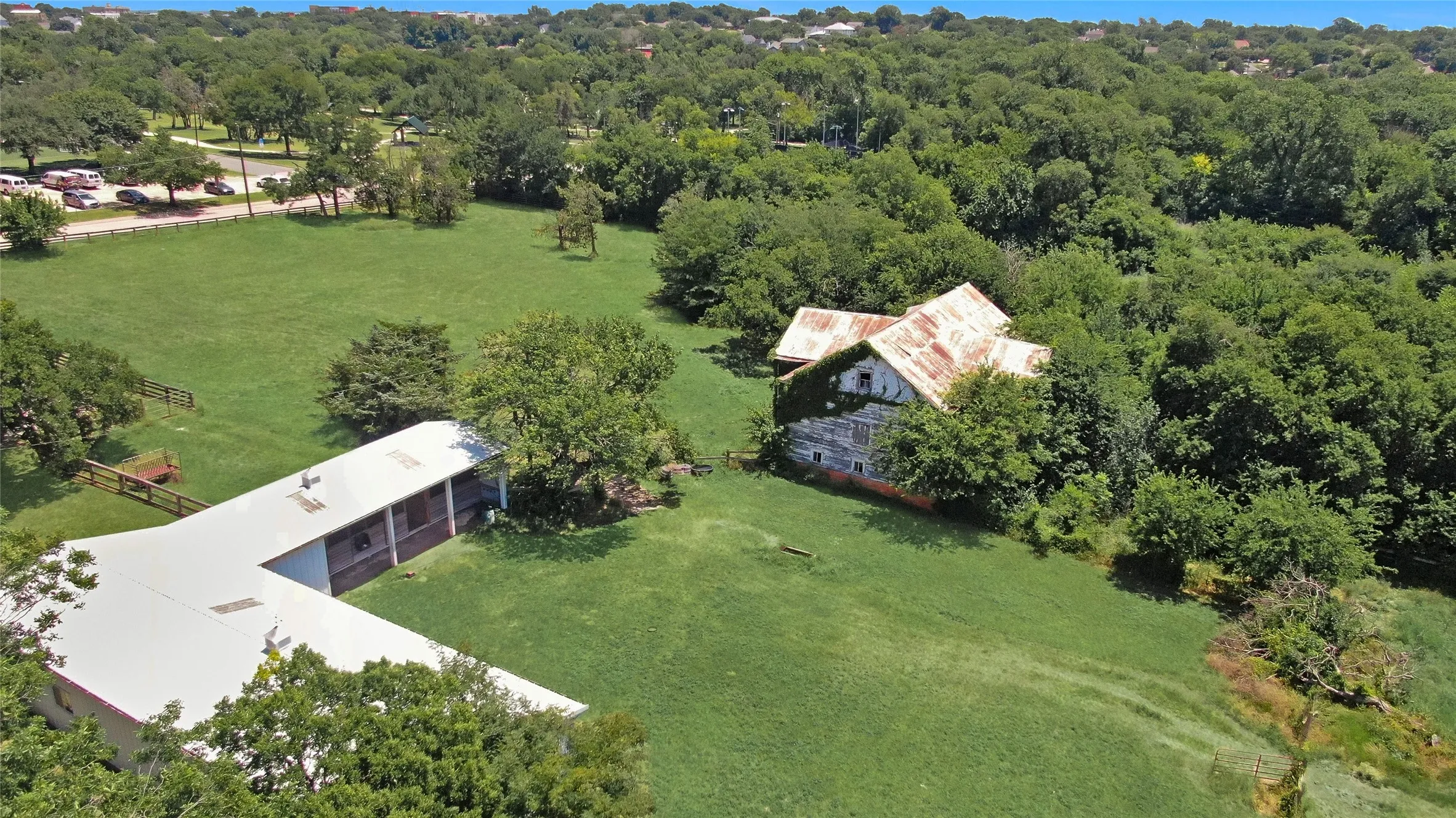 Expansive green grounds featuring a large L-shaped building with a metal roof and a historic barn with a weathered metal roof