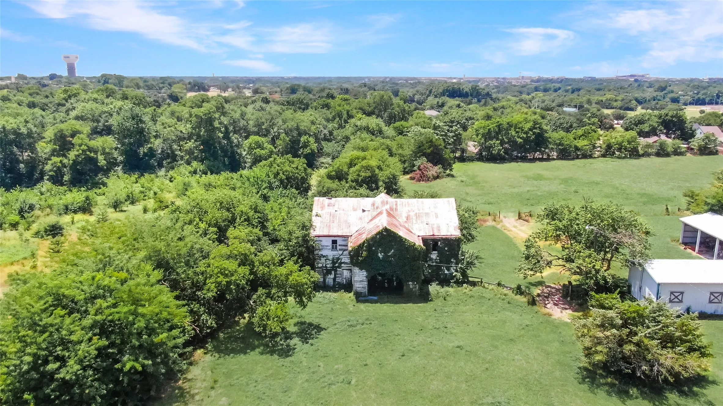 Expansive property featuring a central structure with a weathered metal roof and climbing vines