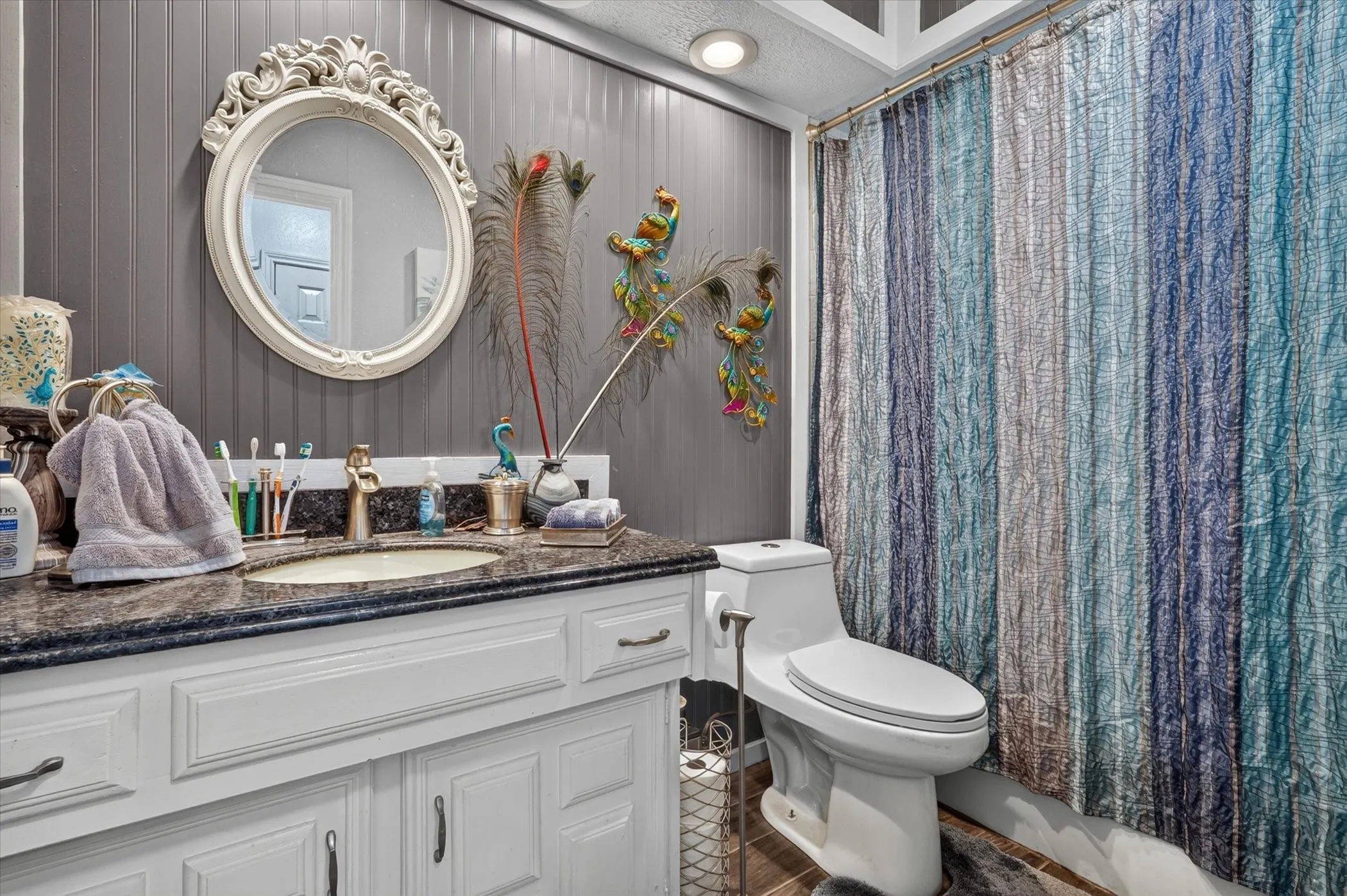 Bathroom featuring a white vanity with a dark countertop, an undermount sink, a decorative framed mirror, and beadboard wall paneling