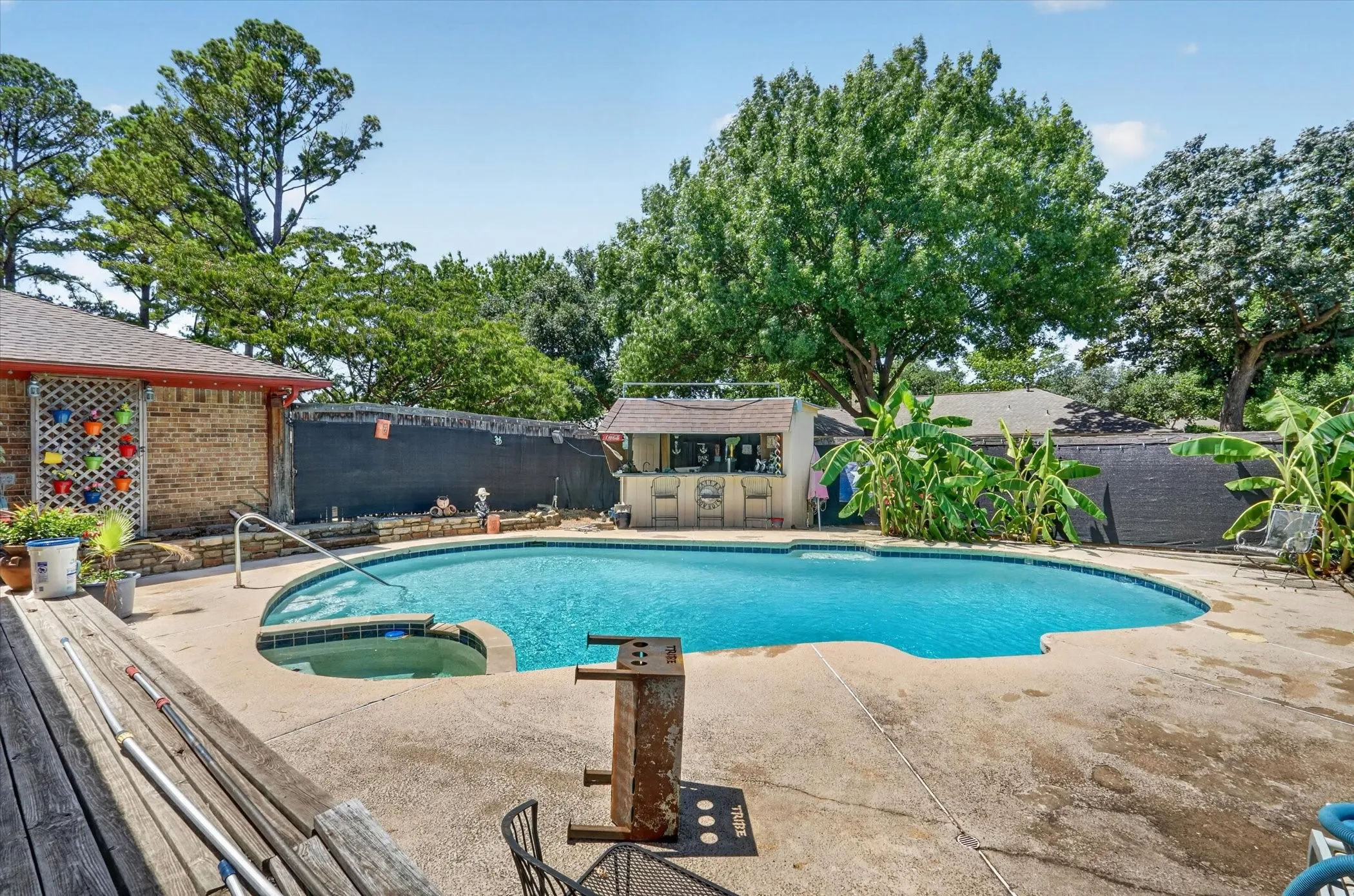 Resort-style backyard featuring a kidney-shaped swimming pool with an integrated spa, expansive concrete pool decking, and a dedicated pool house with a bar