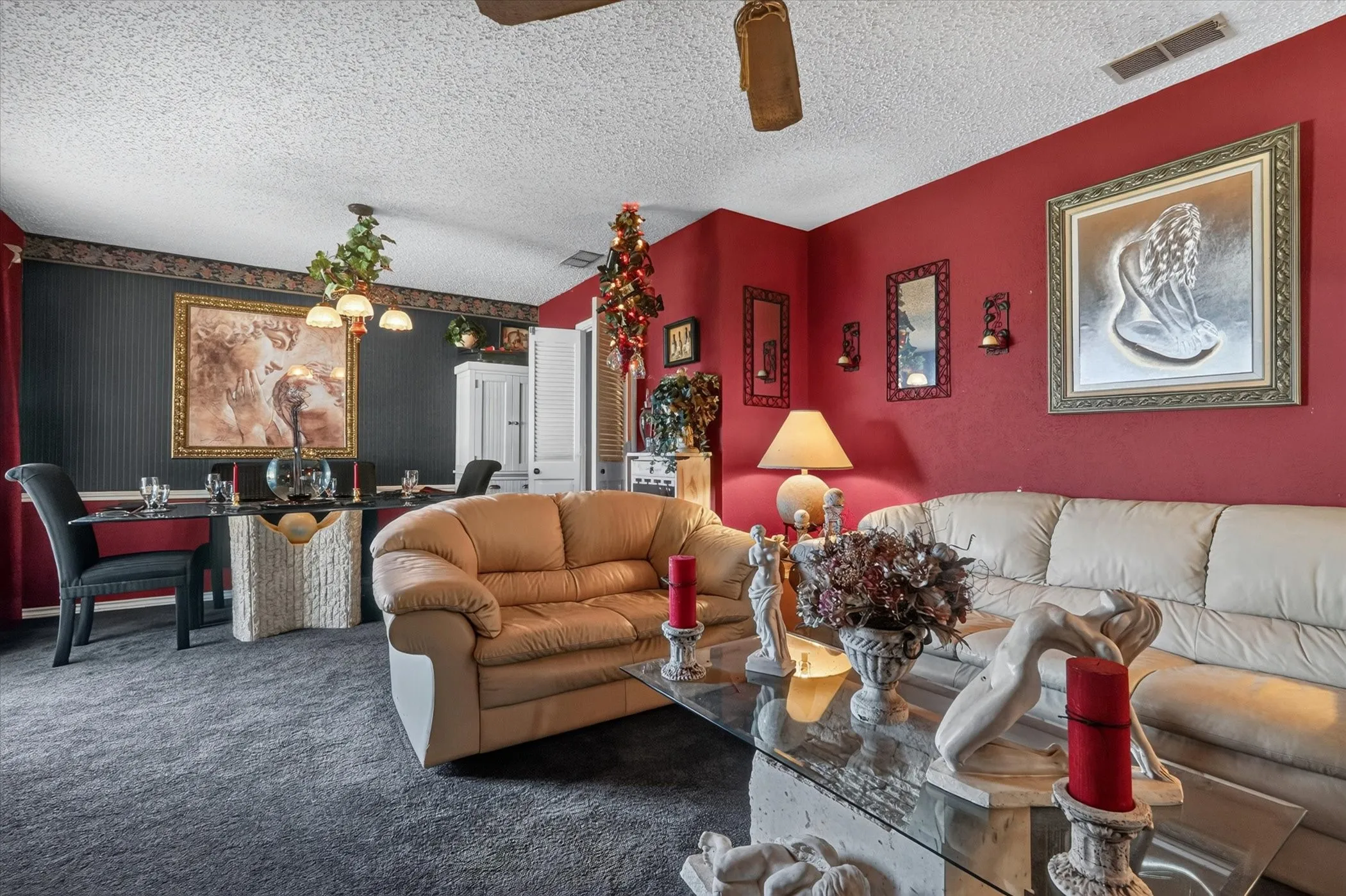 Open concept living and dining area featuring red accent walls, textured dark gray carpeting, and a popcorn ceiling