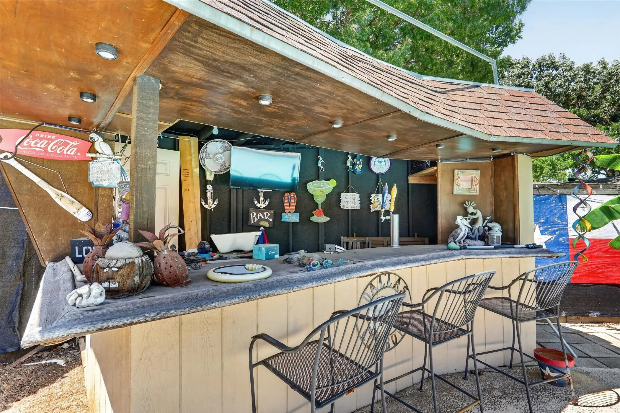 Outdoor bar structure featuring a shingled roof, wood-finish ceiling with recessed lighting, and a solid bar top