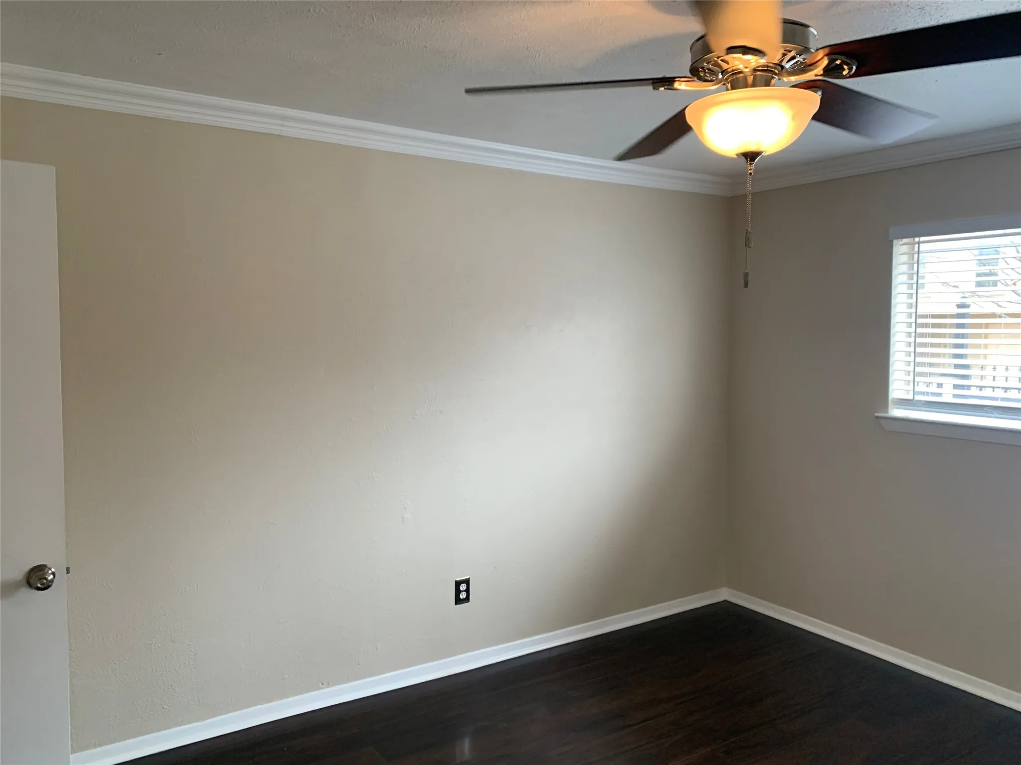Room featuring wood-finish flooring, neutral wall tones, crown molding, and a ceiling fan with integrated lighting