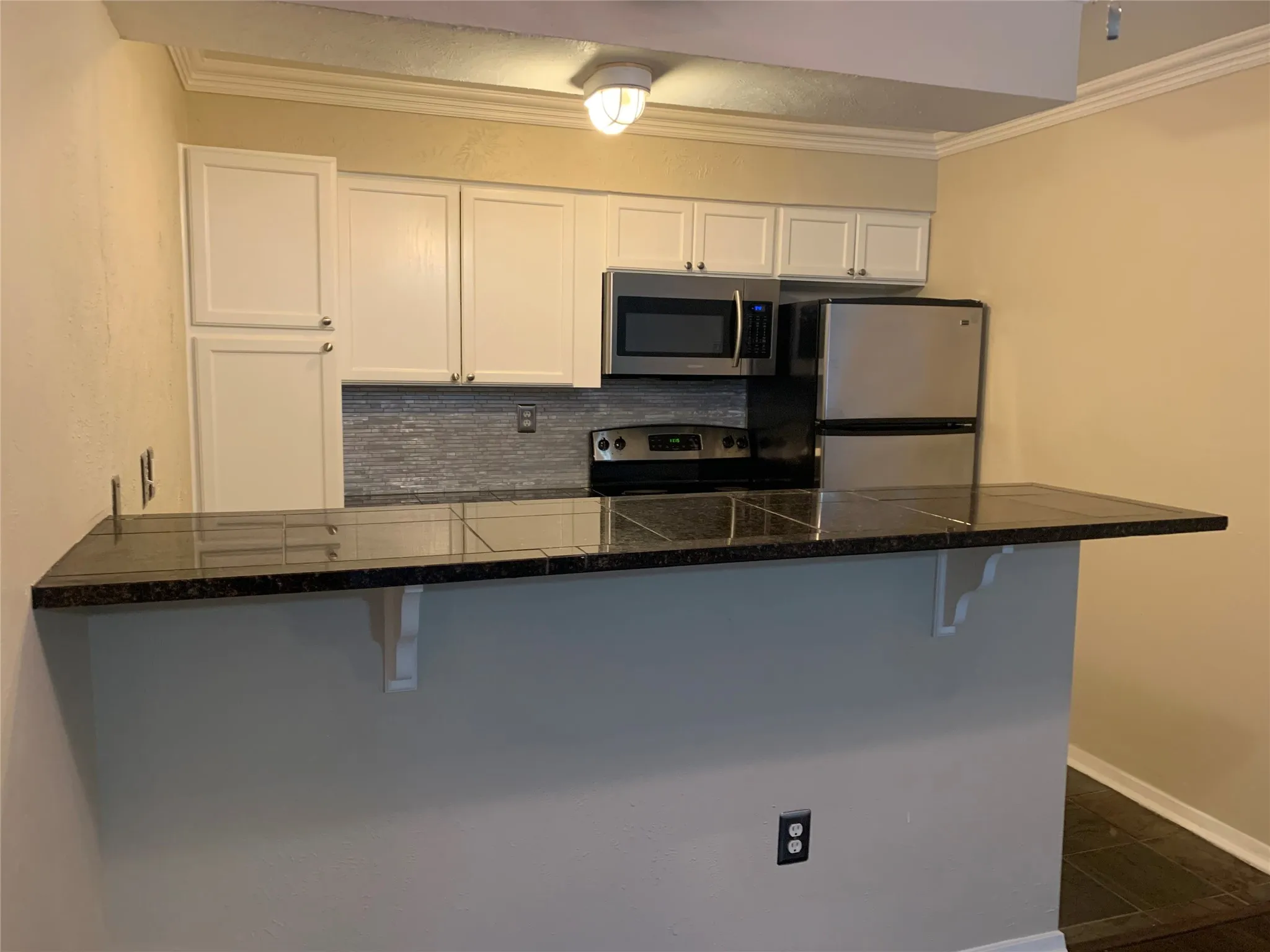 Kitchen bar with dark tile countertop, white cabinetry, and stainless steel appliances