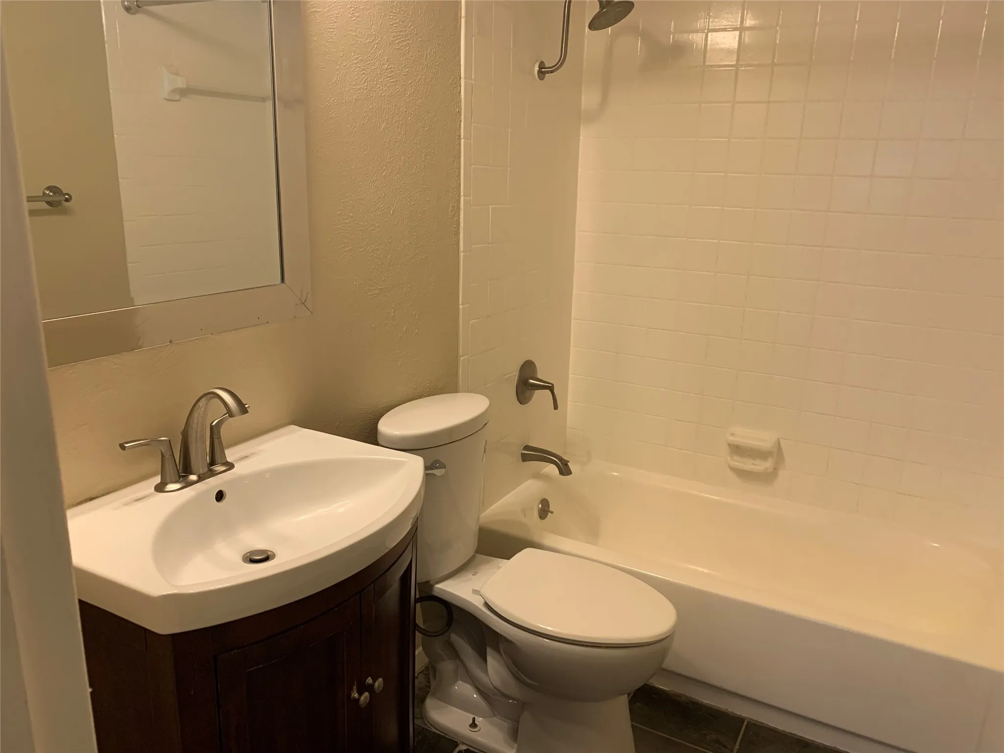 Bathroom featuring a white ceramic bathtub with tiled surround, a toilet, and a vanity with a white basin and dark wood-finish cabinetry