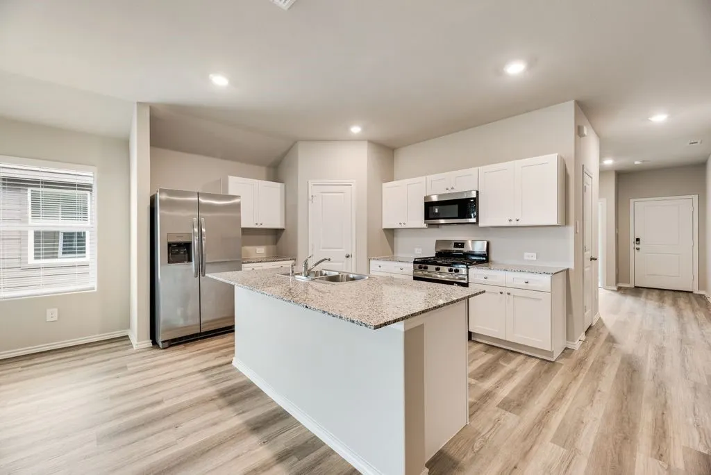 Modern kitchen featuring a central island, stainless steel appliances, white cabinetry, granite countertops, and wood-finish flooring