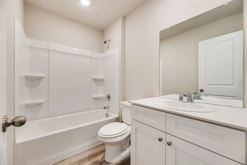 Bathroom featuring a white vanity with an integrated sink, chrome fixtures, and a white tub with shower surround