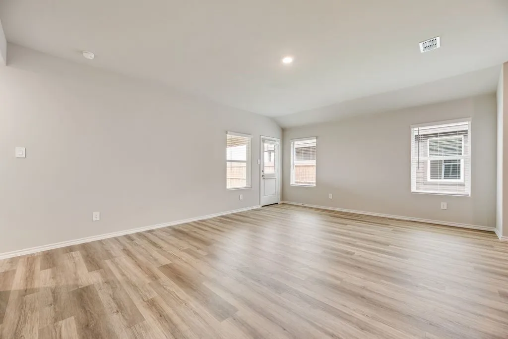 Spacious room featuring wood-finish flooring, light-toned walls, multiple windows with blinds, recessed lighting, and a white door with a window pane
