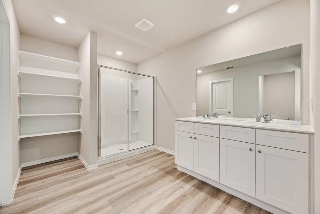 Full bathroom featuring a double vanity with white cabinetry, a large frameless mirror, a glass-enclosed shower, and built-in shelving