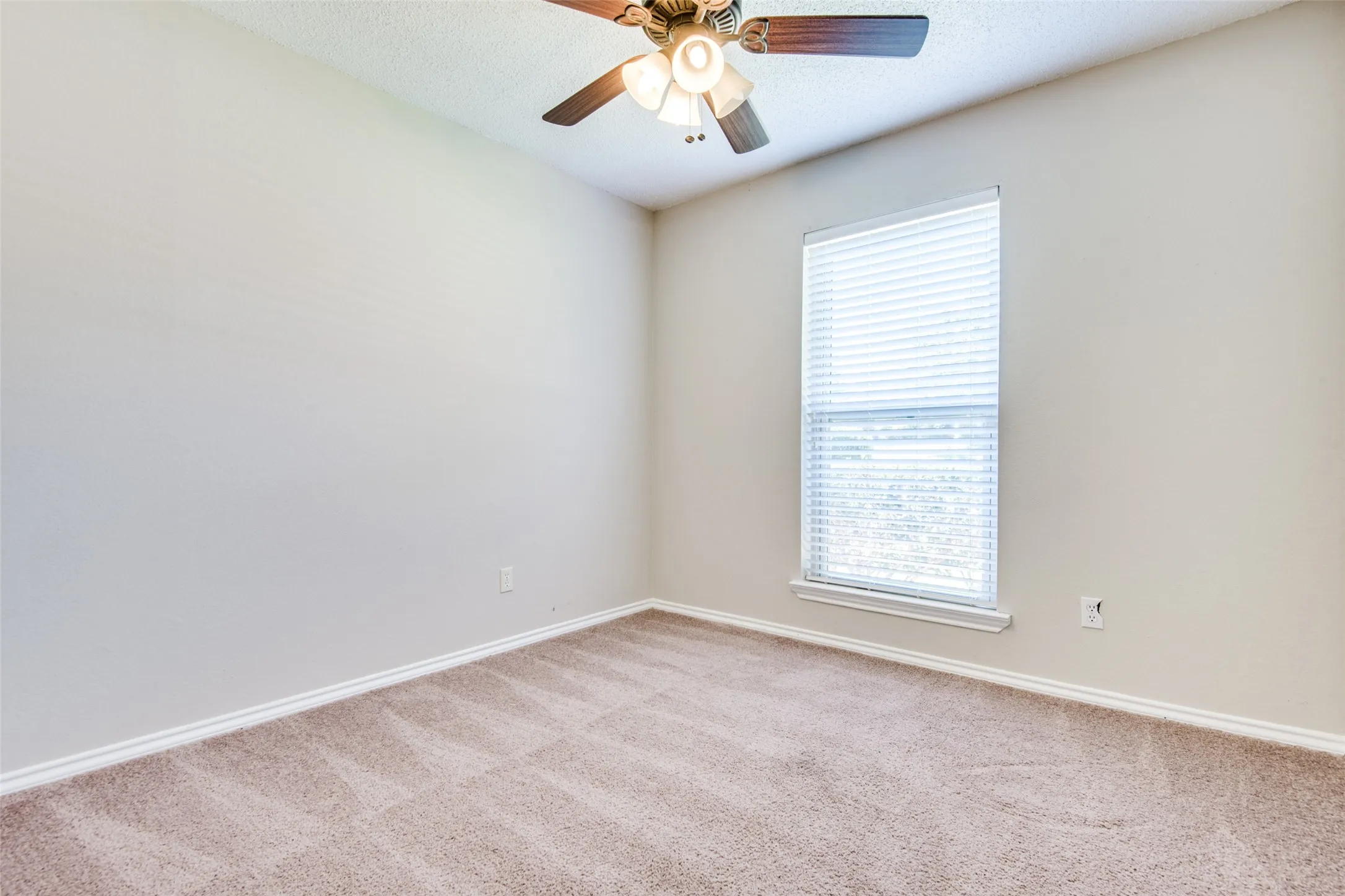 Neutral-toned room featuring a single window with blinds, carpet flooring, a ceiling fan with light fixture, and white trim