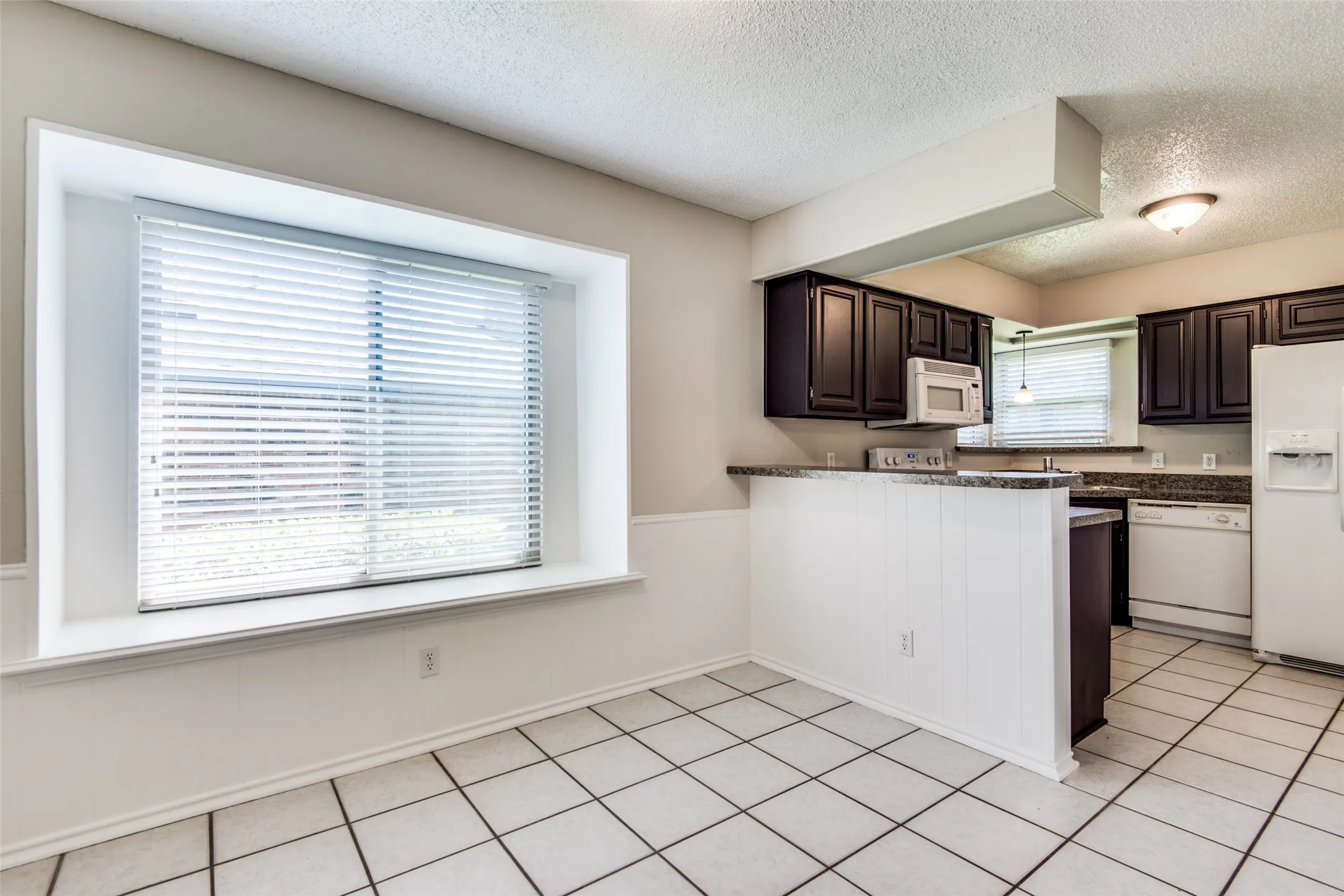 Kitchen and dining area featuring dark wood cabinetry, light-toned countertops, and white appliances