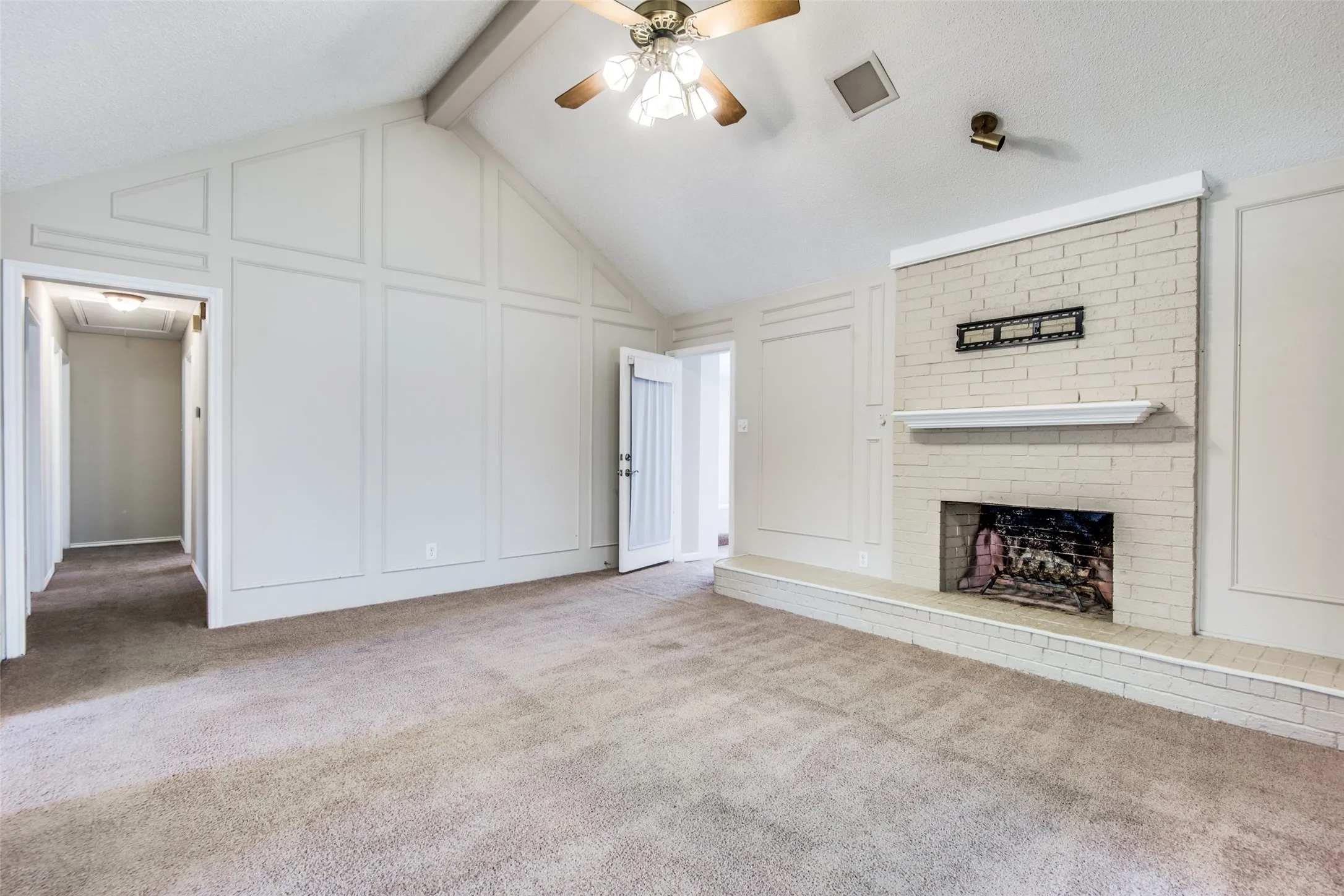 Living room featuring a vaulted ceiling with a ceiling fan, a painted brick fireplace with a mantel, and paneled wall details