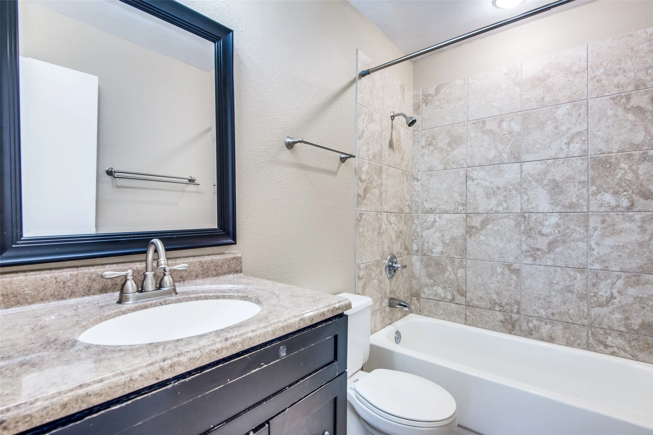 Bathroom featuring a vanity with an integrated sink, framed mirror, and a bathtub with a tiled shower surround