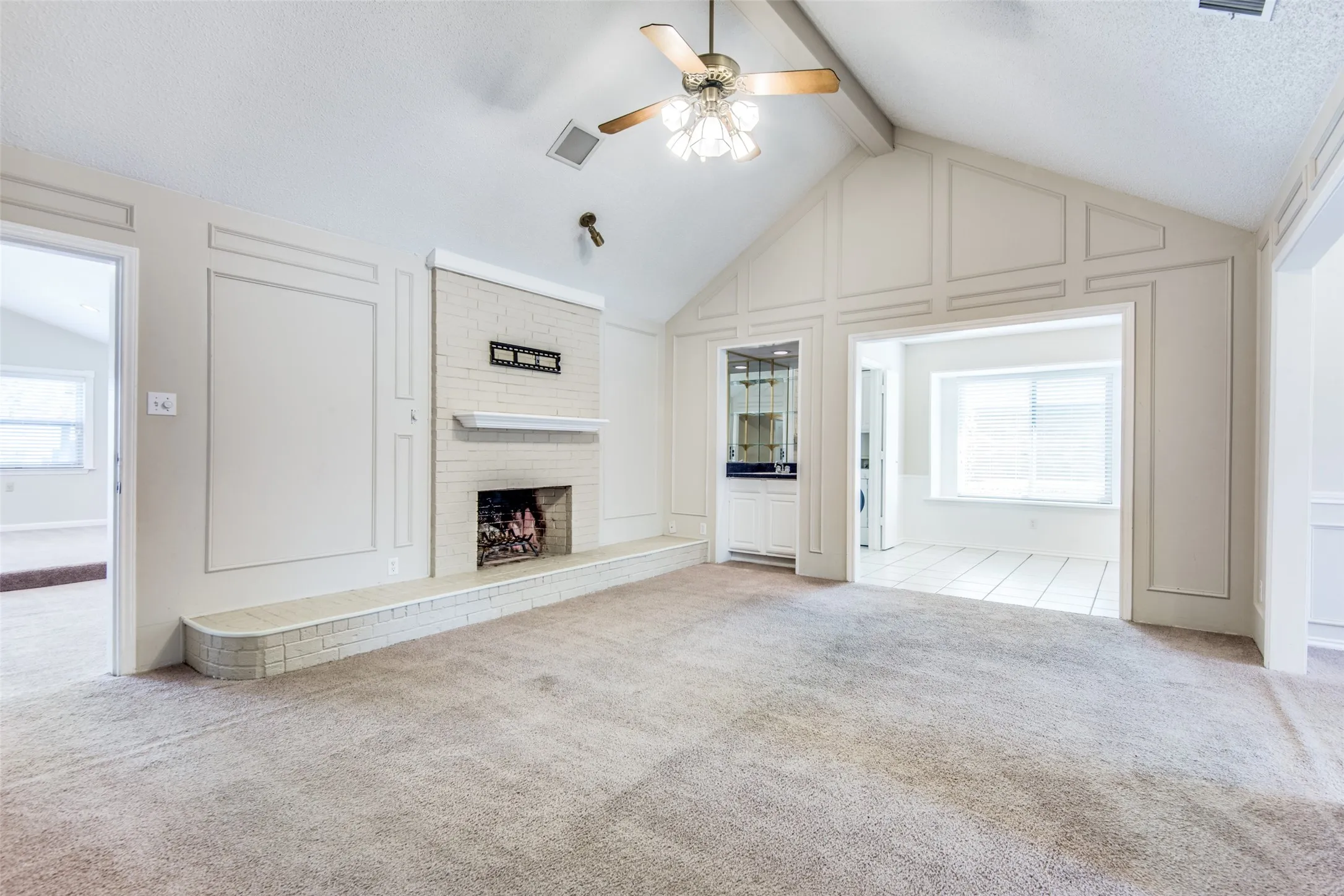 Vaulted ceiling living area featuring a brick fireplace, built-in wet bar, paneling details, and a ceiling fan