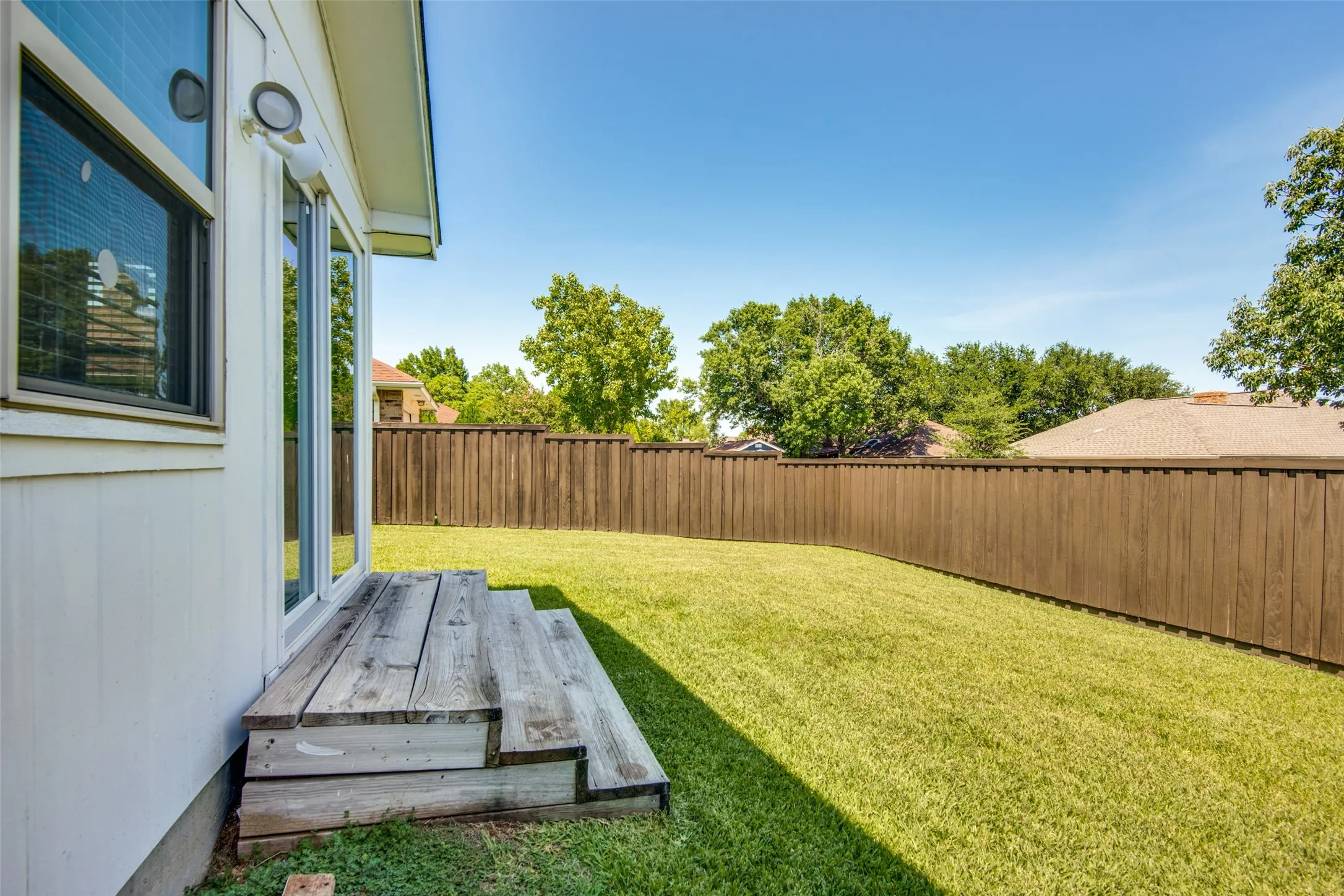 Spacious backyard featuring a wood privacy fence, a manicured lawn, and mature trees