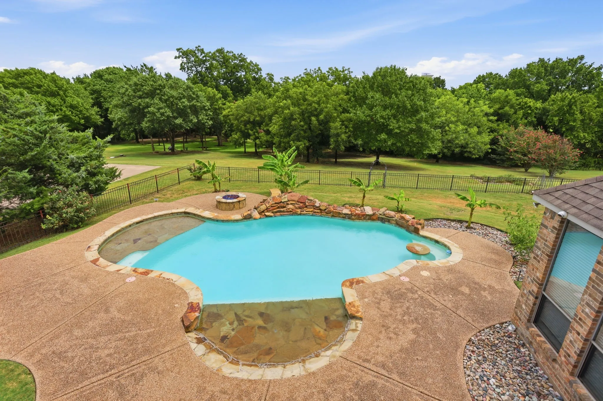 Kidney-shaped swimming pool featuring a rock waterfall, surrounded by an exposed aggregate concrete patio