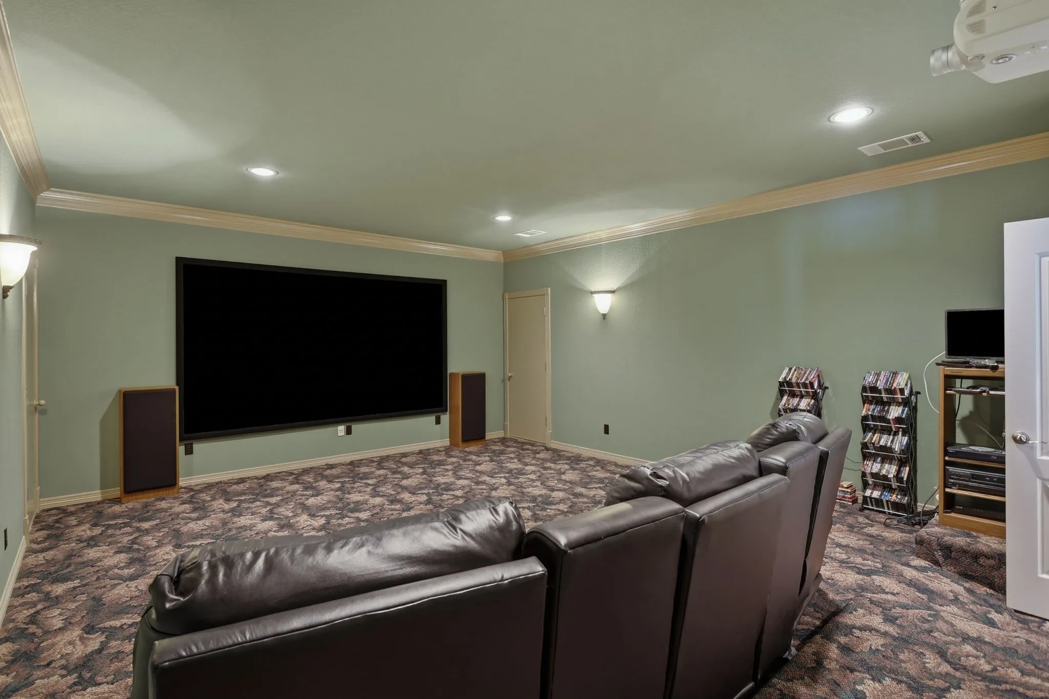 Dedicated media room featuring a large projection screen, recessed ceiling lighting, and wall sconces