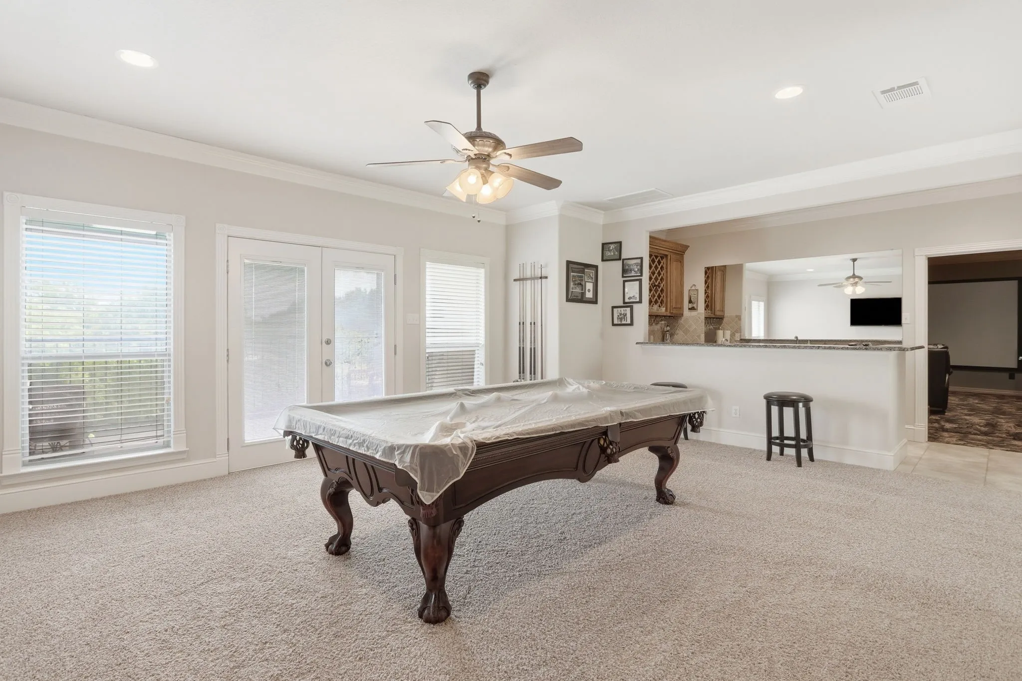 Spacious entertainment room featuring recessed lighting, crown molding, a built-in wet bar with wood cabinetry, and double glass-panel doors