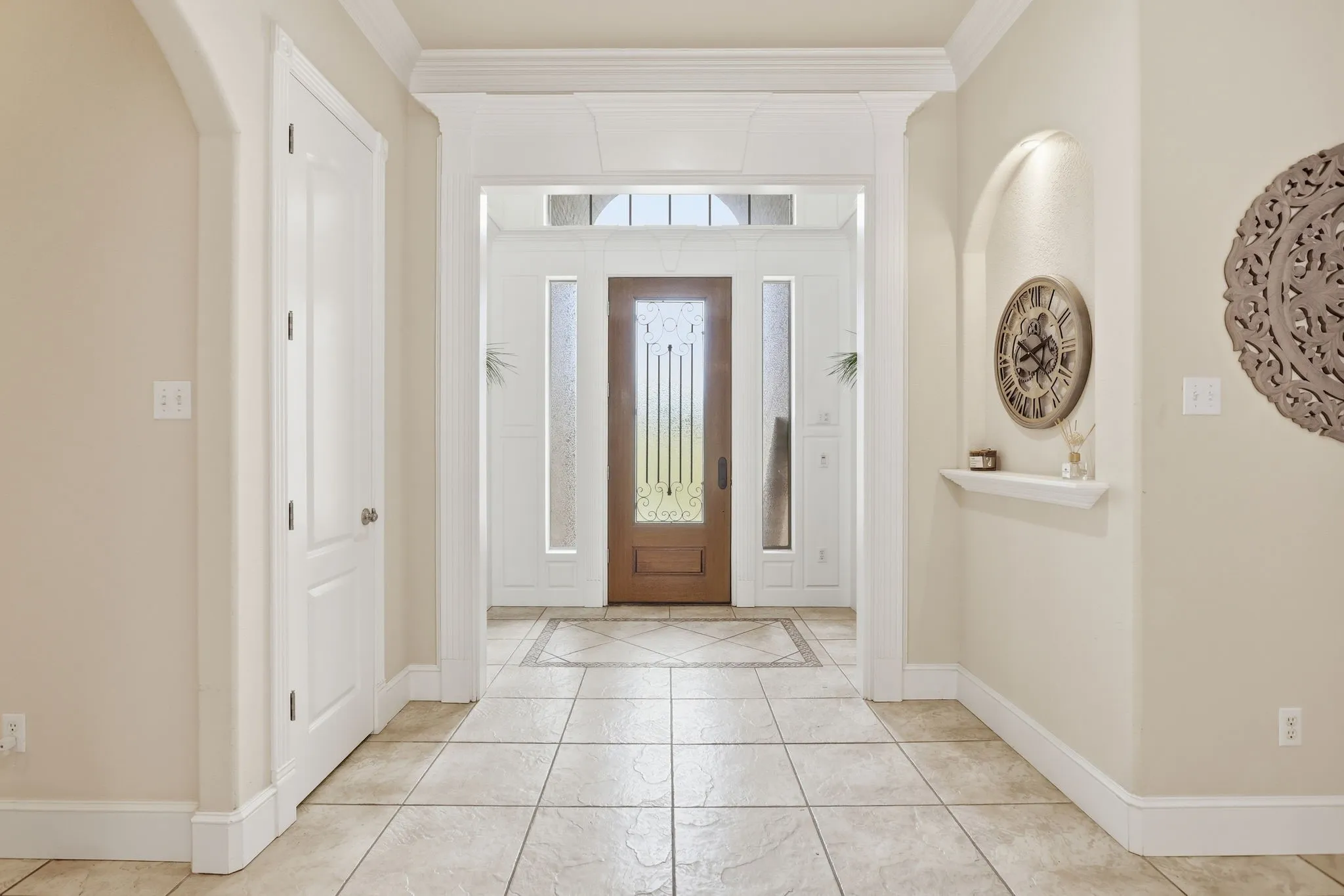 Entry foyer featuring tile flooring with a decorative inlay, an arched wall niche with integrated lighting, a solid wood front door with decorative glass, and sidelight windows with frosted glass