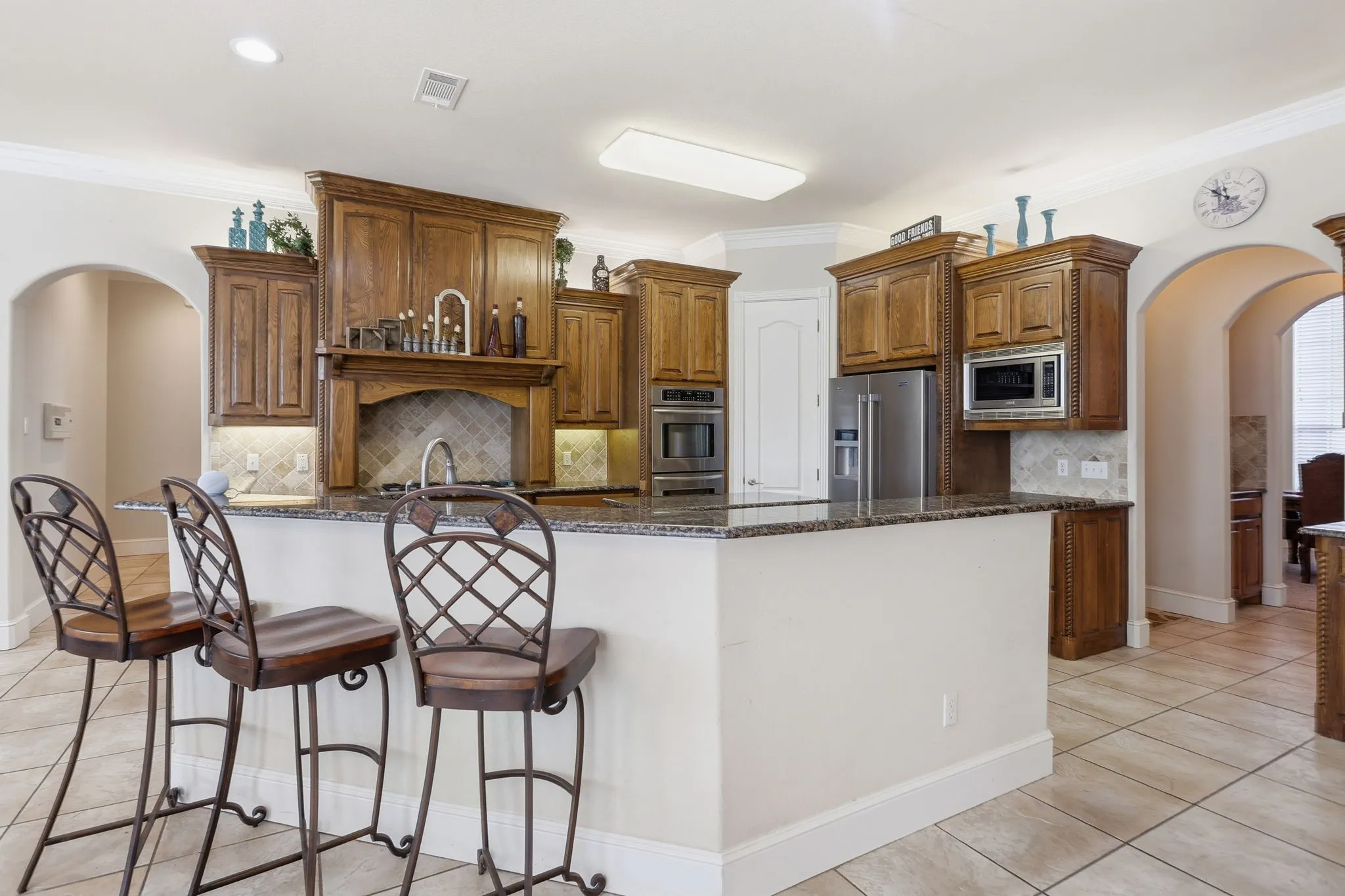 Kitchen featuring wood cabinetry, stainless steel appliances, a tiled backsplash, and a granite-look island with a breakfast bar