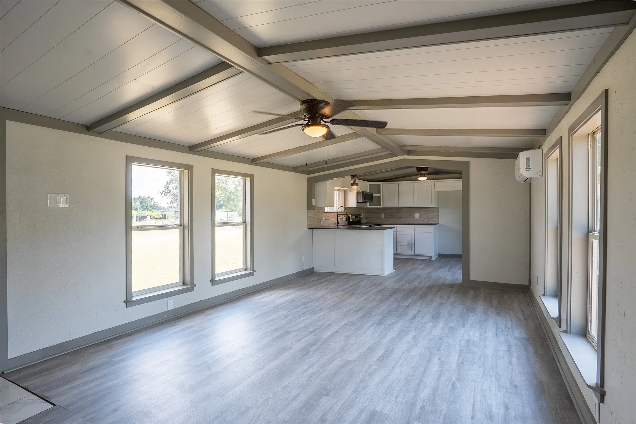 Vaulted ceiling with exposed beams, wood-finish flooring, multiple windows, recessed lighting, and a ceiling fan