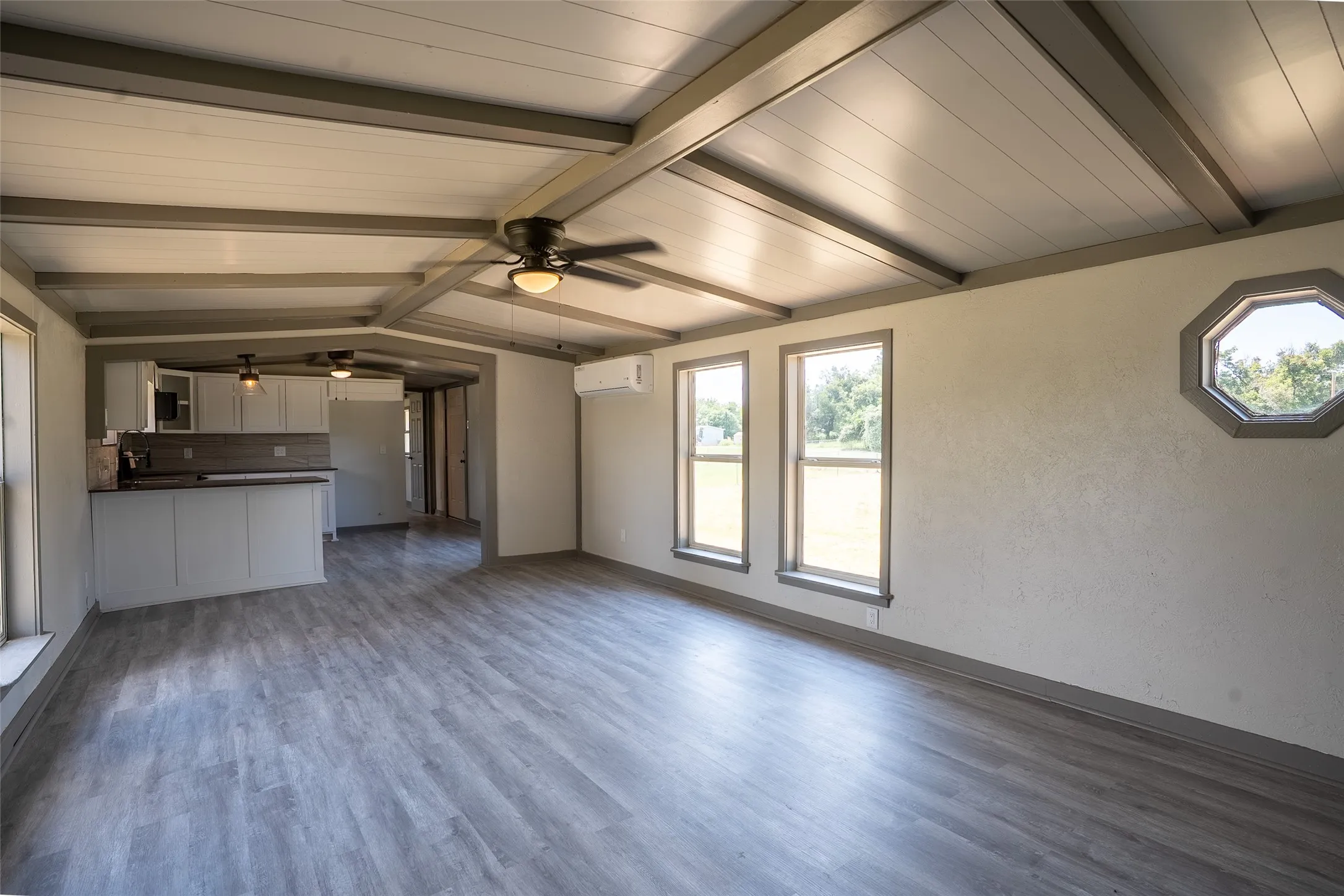 Open concept living space featuring wood-finish flooring, exposed beam ceiling, and a ceiling fan with integrated lighting