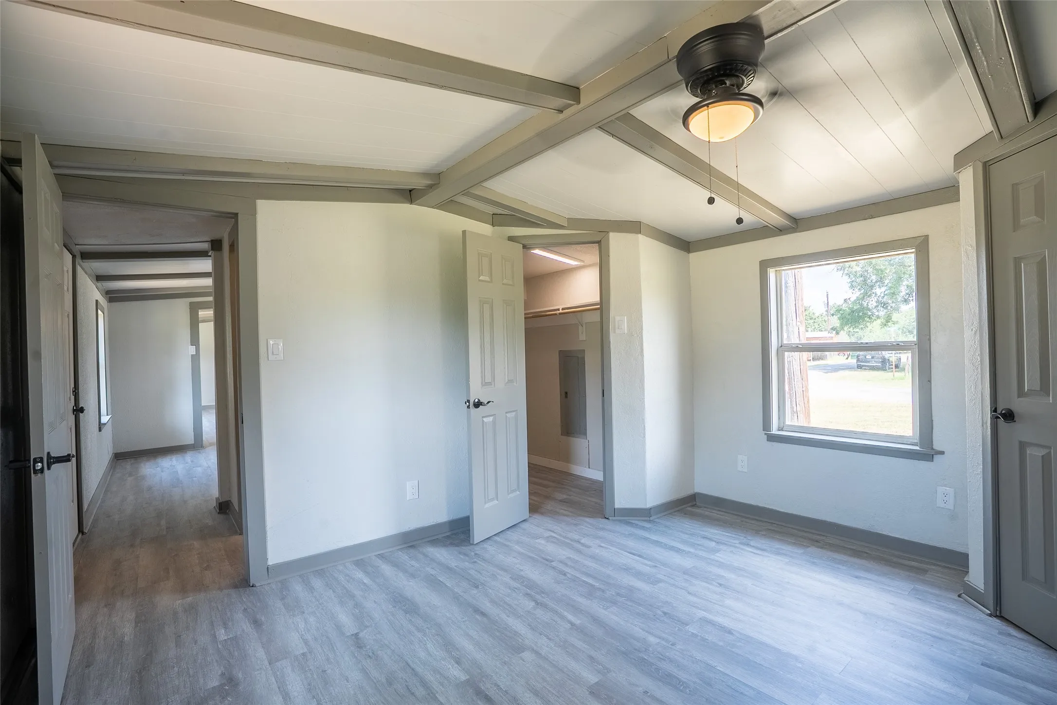 Spacious room featuring wood-finish flooring, a ceiling fan with integrated lighting, and a large window with trim