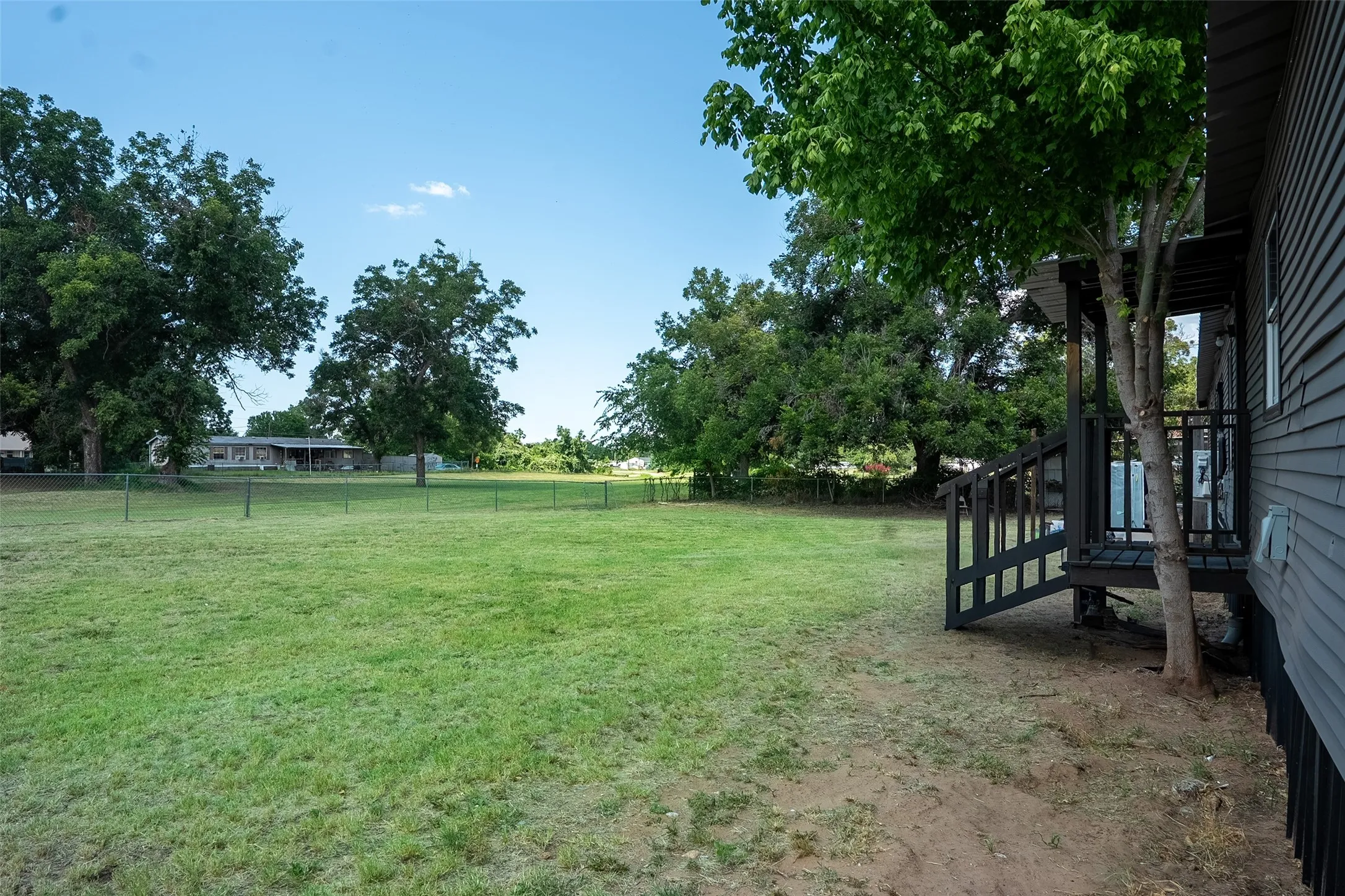 Expansive lawn area featuring mature trees and a chain-link fence