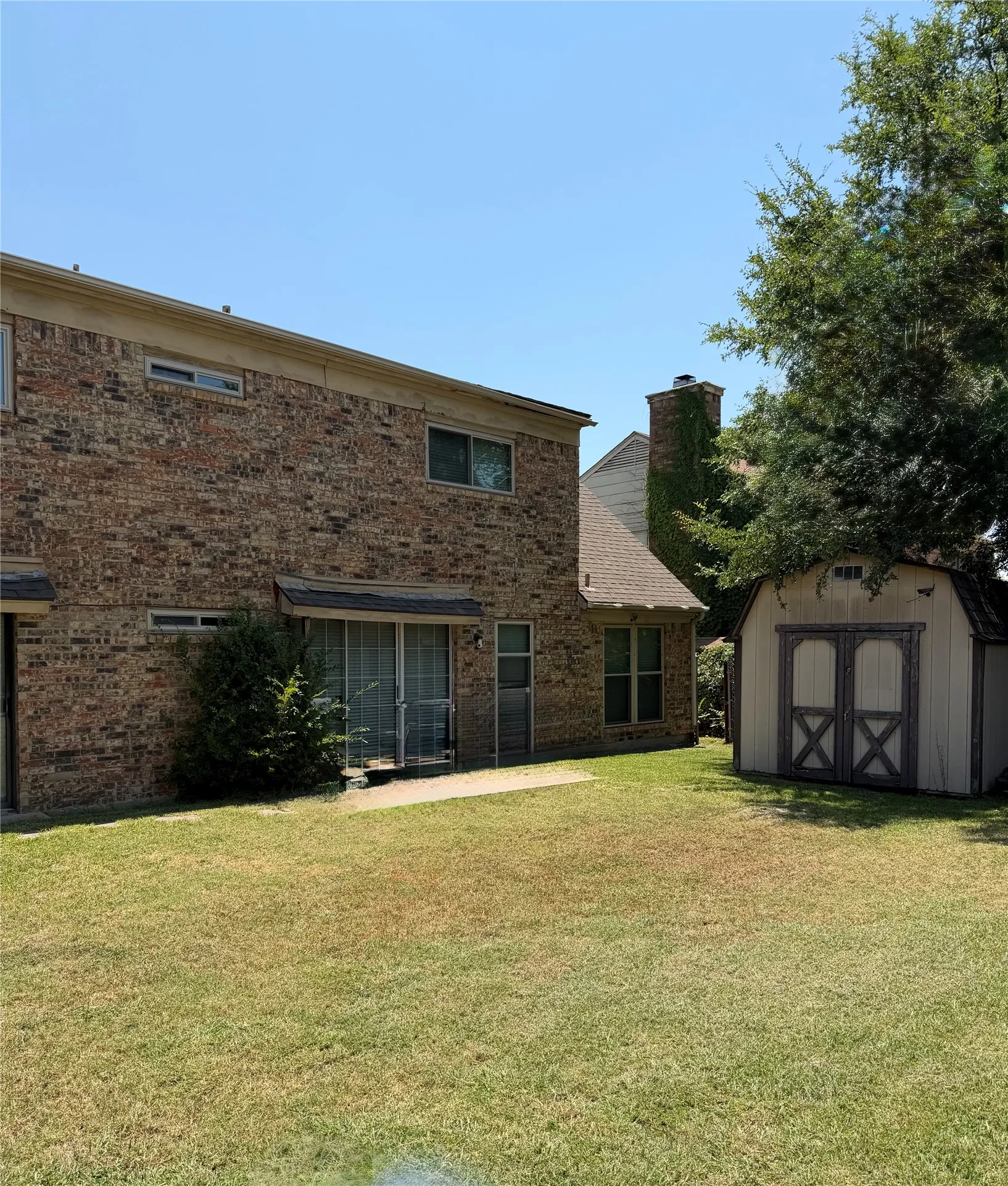 Expansive backyard featuring a storage shed with double doors, a concrete patio, and mature trees