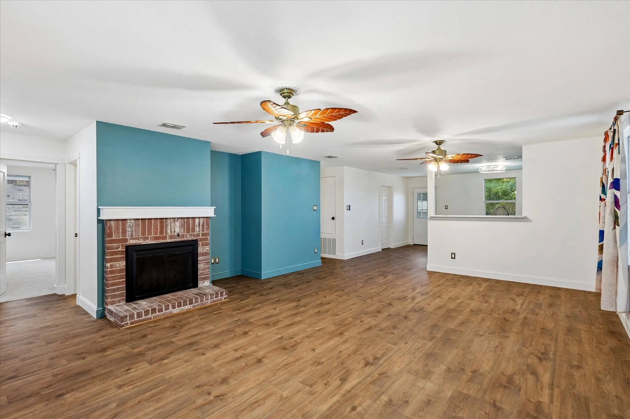 Open living area featuring wood-finish flooring, a brick fireplace with a white mantel, and ceiling fans