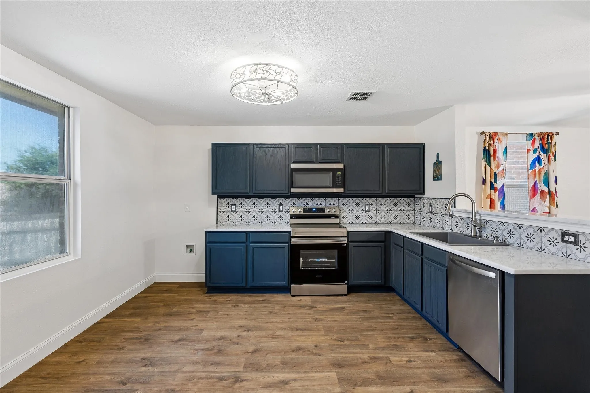 Kitchen featuring wood-finish flooring, dark blue cabinetry, stainless steel appliances, patterned tile backsplash, and light-colored countertops