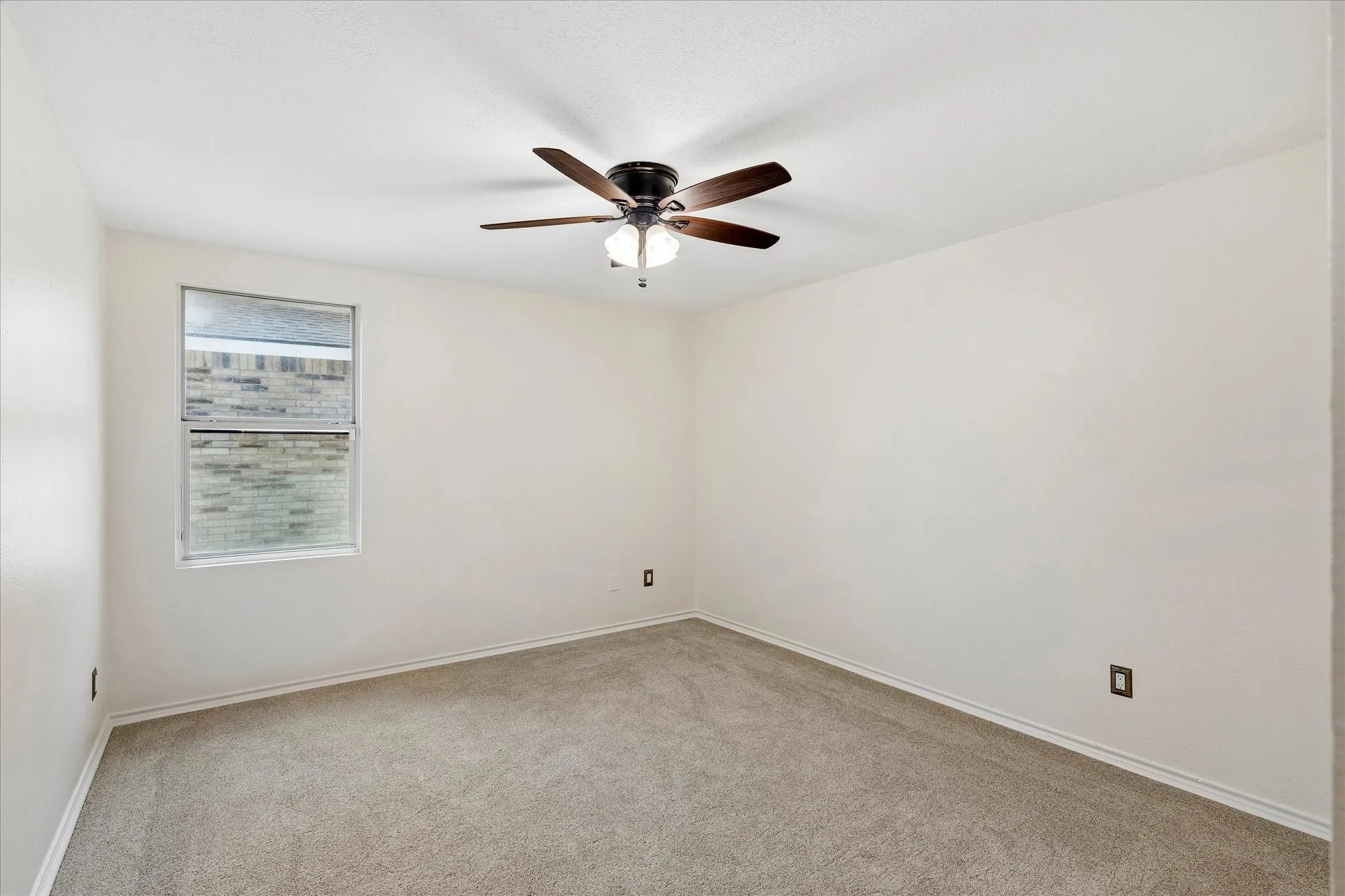 Spacious room featuring neutral carpeting, light-toned walls, and a ceiling fan with integrated lighting