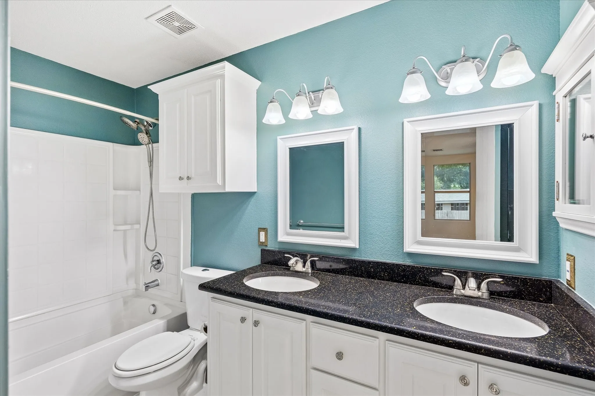 Bathroom featuring a dual vanity with dark speckled countertops, undermount sinks, and white shaker-style cabinetry