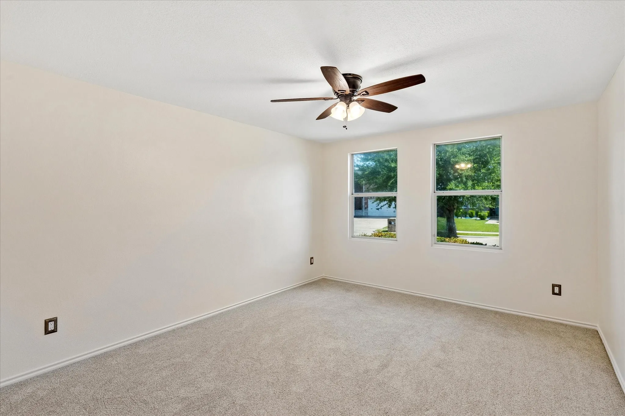 Spacious room featuring neutral carpet, a ceiling fan with integrated lighting, and two large windows providing natural illumination