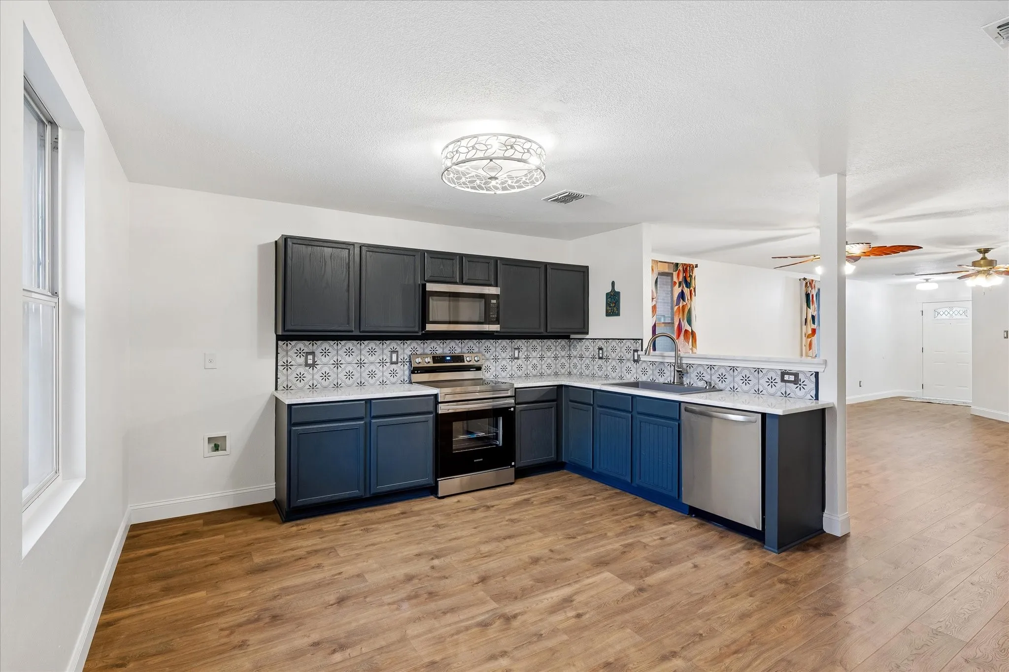 Modern kitchen featuring dark cabinetry, stainless steel appliances, decorative tiled backsplash, light countertops, and wood-finish flooring