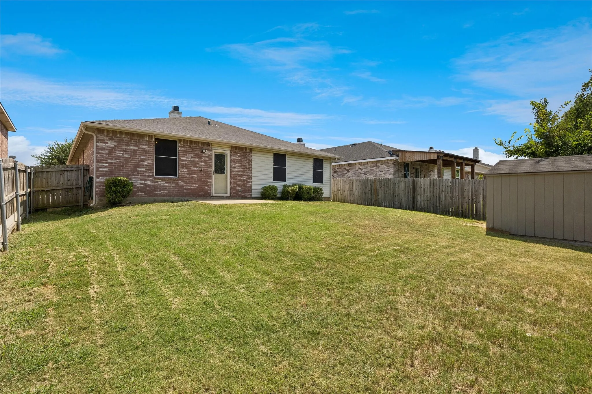 Expansive backyard featuring a manicured lawn, full privacy fencing, and an integrated storage shed