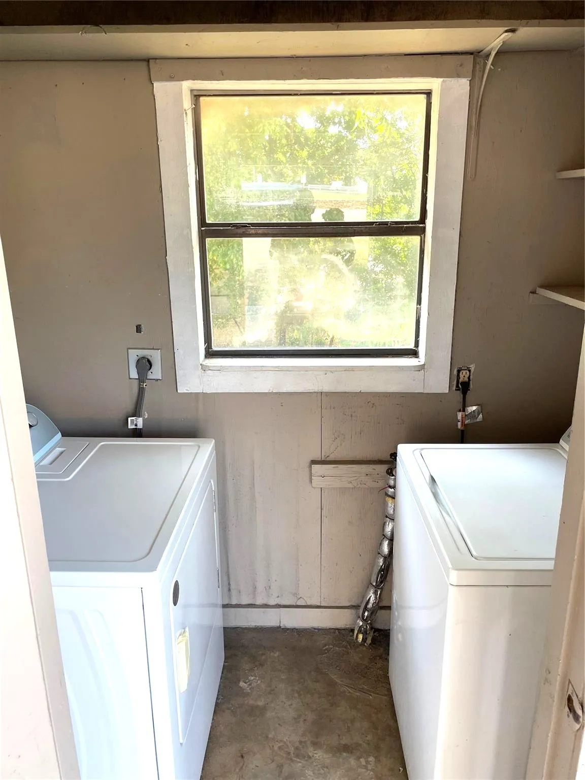 Utility room featuring a window, open shelving, and concrete flooring