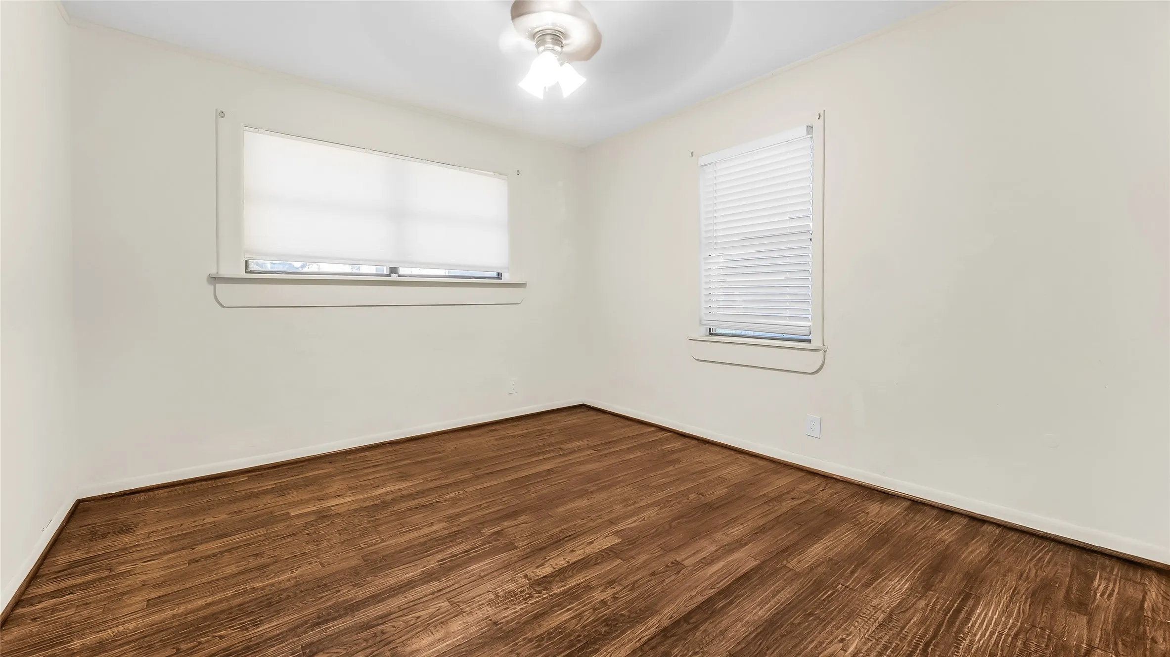 Wood-finish flooring throughout, bright white walls, and a ceiling fan with integrated lighting