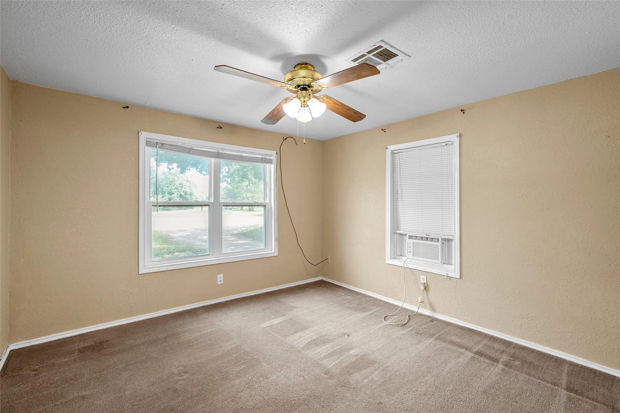 Neutral tone walls featuring two distinct windows, brown carpet, and a ceiling fan with light fixture