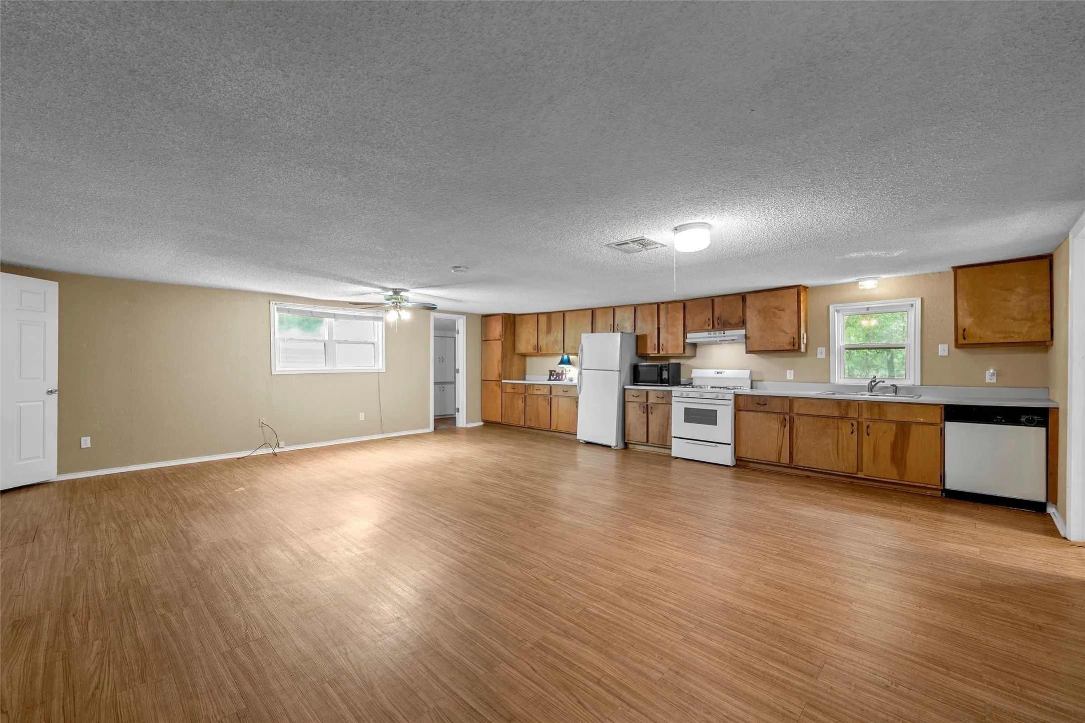 Open-concept living space featuring wood-finish flooring, a full kitchen with integrated appliances, wood cabinetry, and a ceiling fan