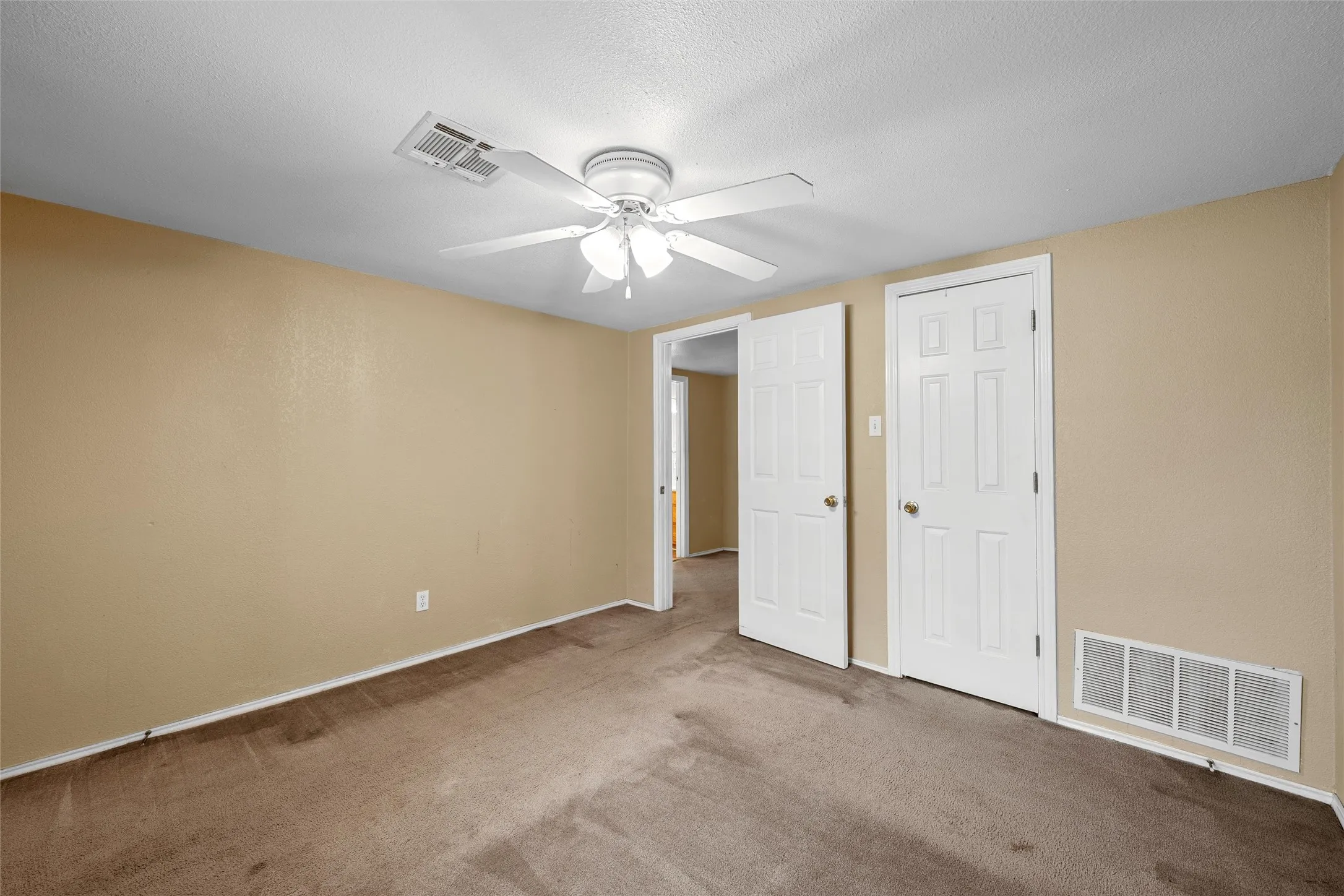 Carpeted room with a ceiling fan, light beige walls, and white trim