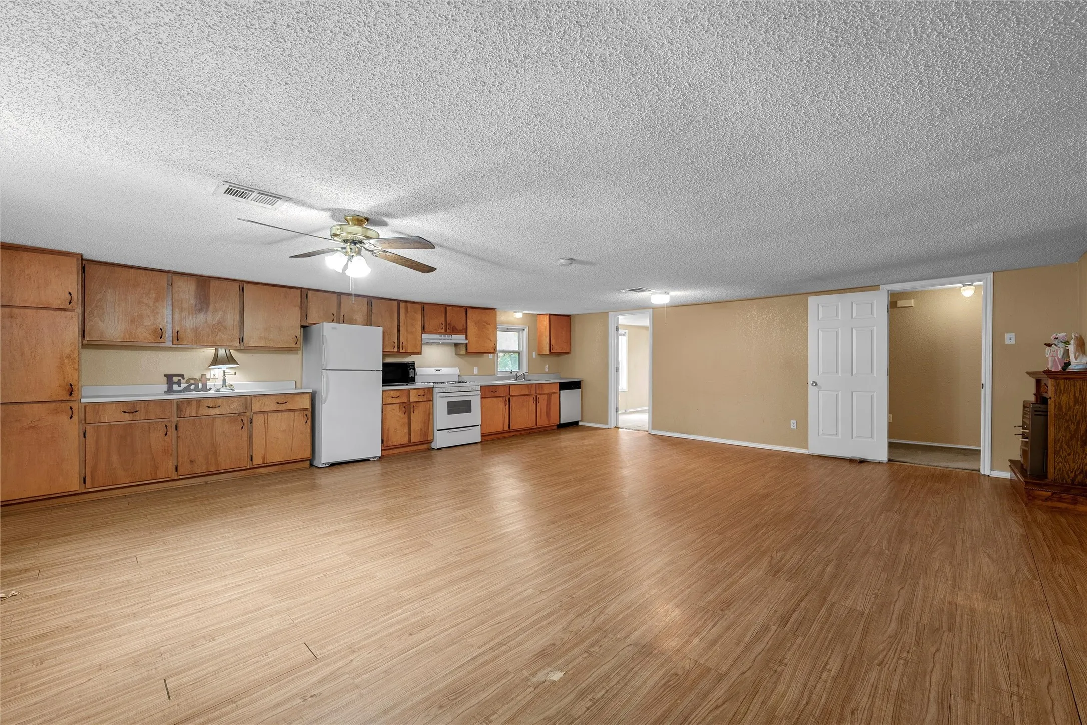 Open-concept space featuring wood-finish flooring, a full kitchen with wood cabinetry and white appliances, a ceiling fan, and neutral wall paint