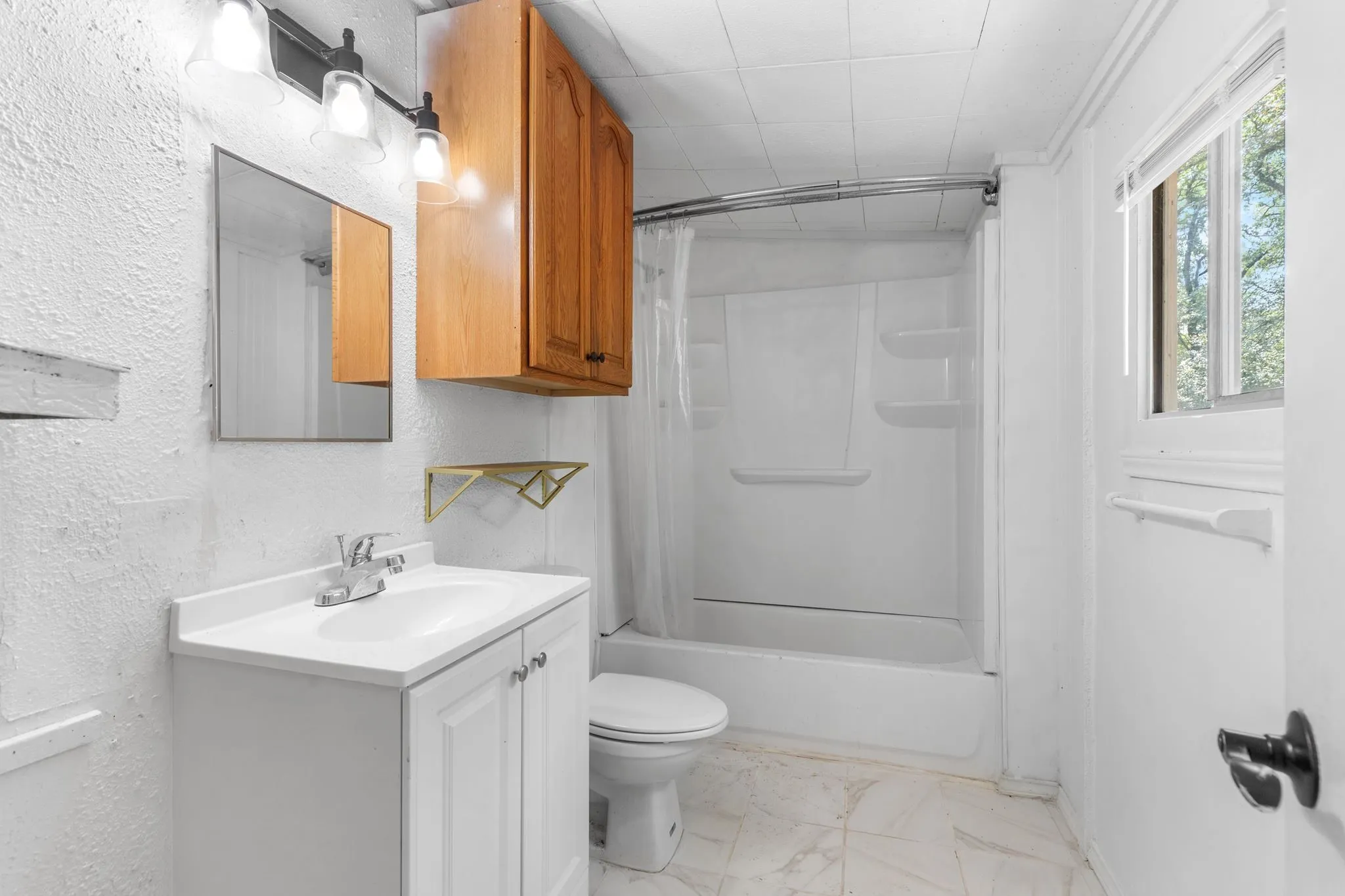 White vanity with integrated sink, chrome faucet, wall-mounted mirror, overhead lighting fixture, and a white shower-tub combination
walk-in closet on opposite side of bath
