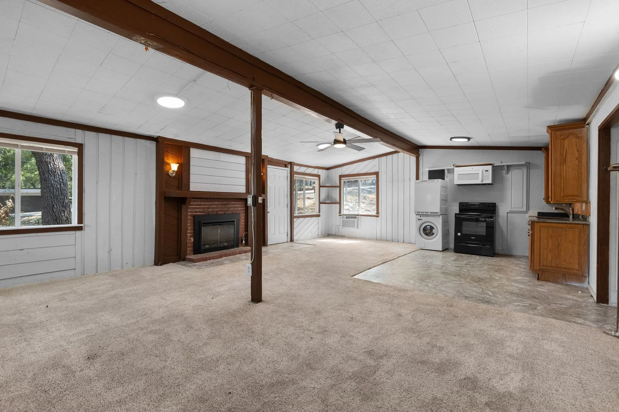Spacious open-concept living area featuring neutral carpet flooring, exposed wood beam support structure, and recessed ceiling lighting