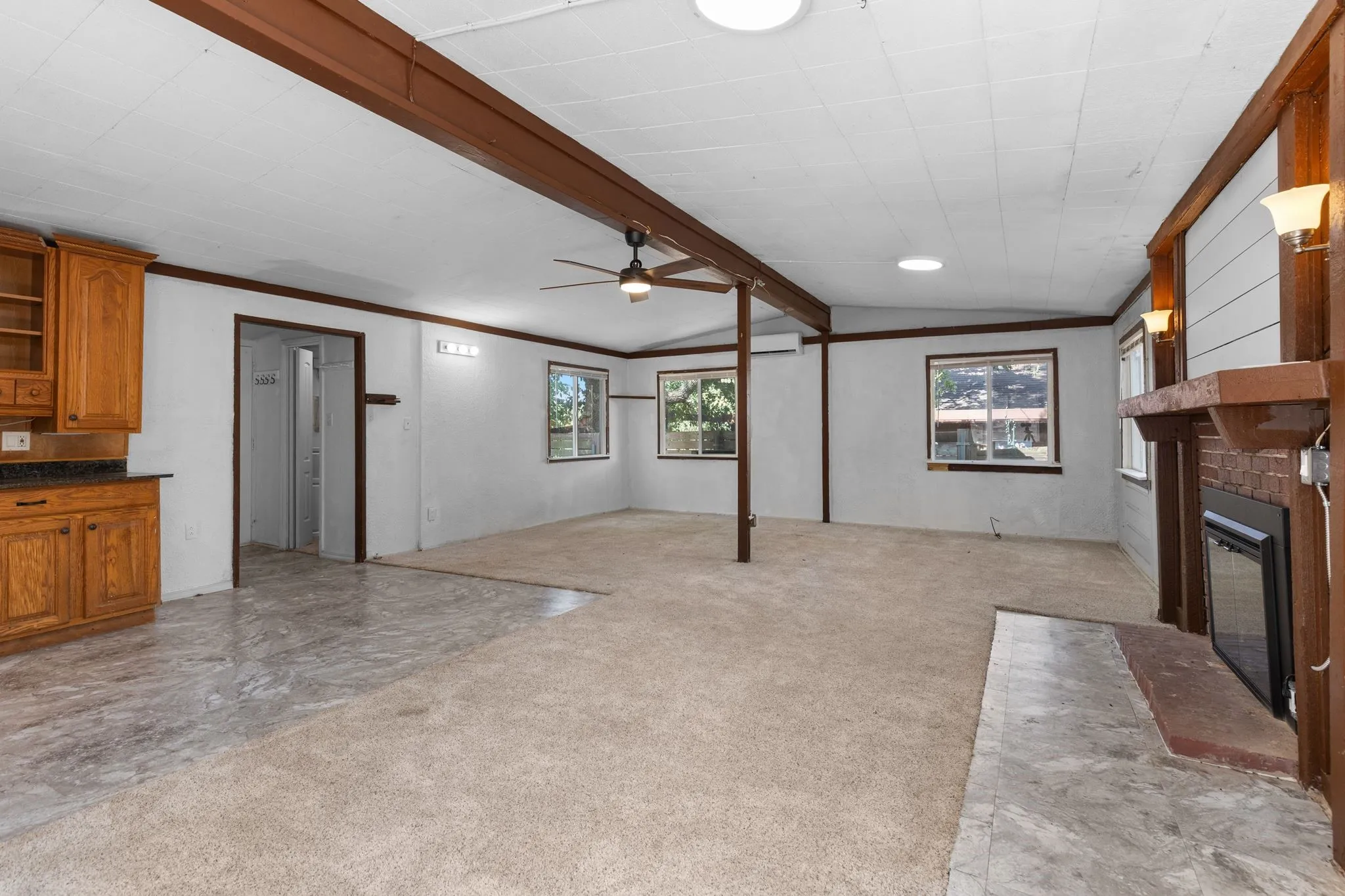 Living space featuring a built-in fireplace, ceiling fan, multiple windows, and a combination of carpet and tiled flooring