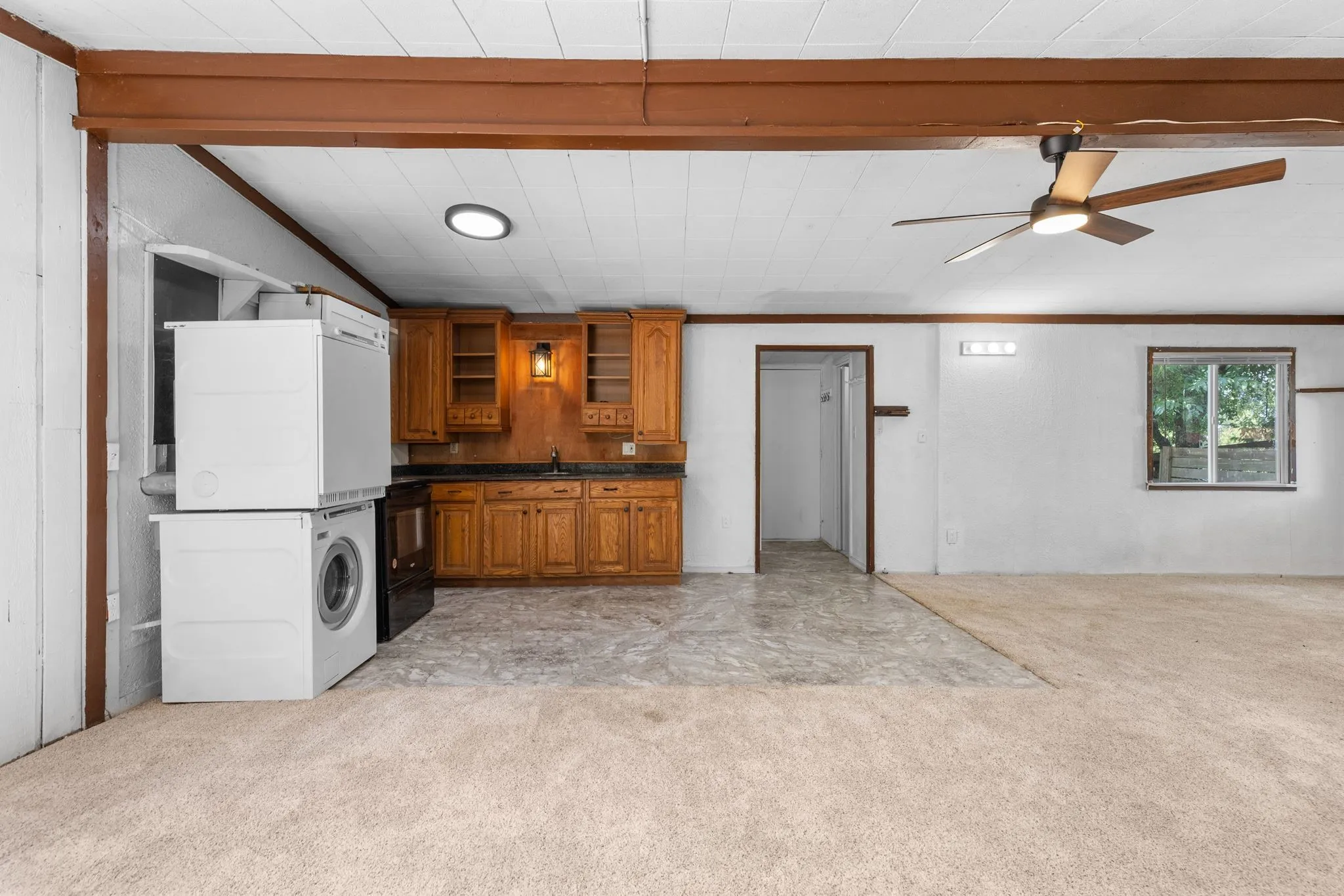 Spacious open-concept living area with wood-beam ceiling detail and ceiling fan