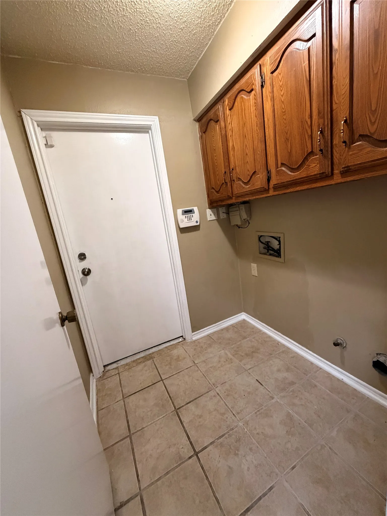 Utility area featuring wood-finish cabinetry, neutral wall paint, and ceramic tile flooring